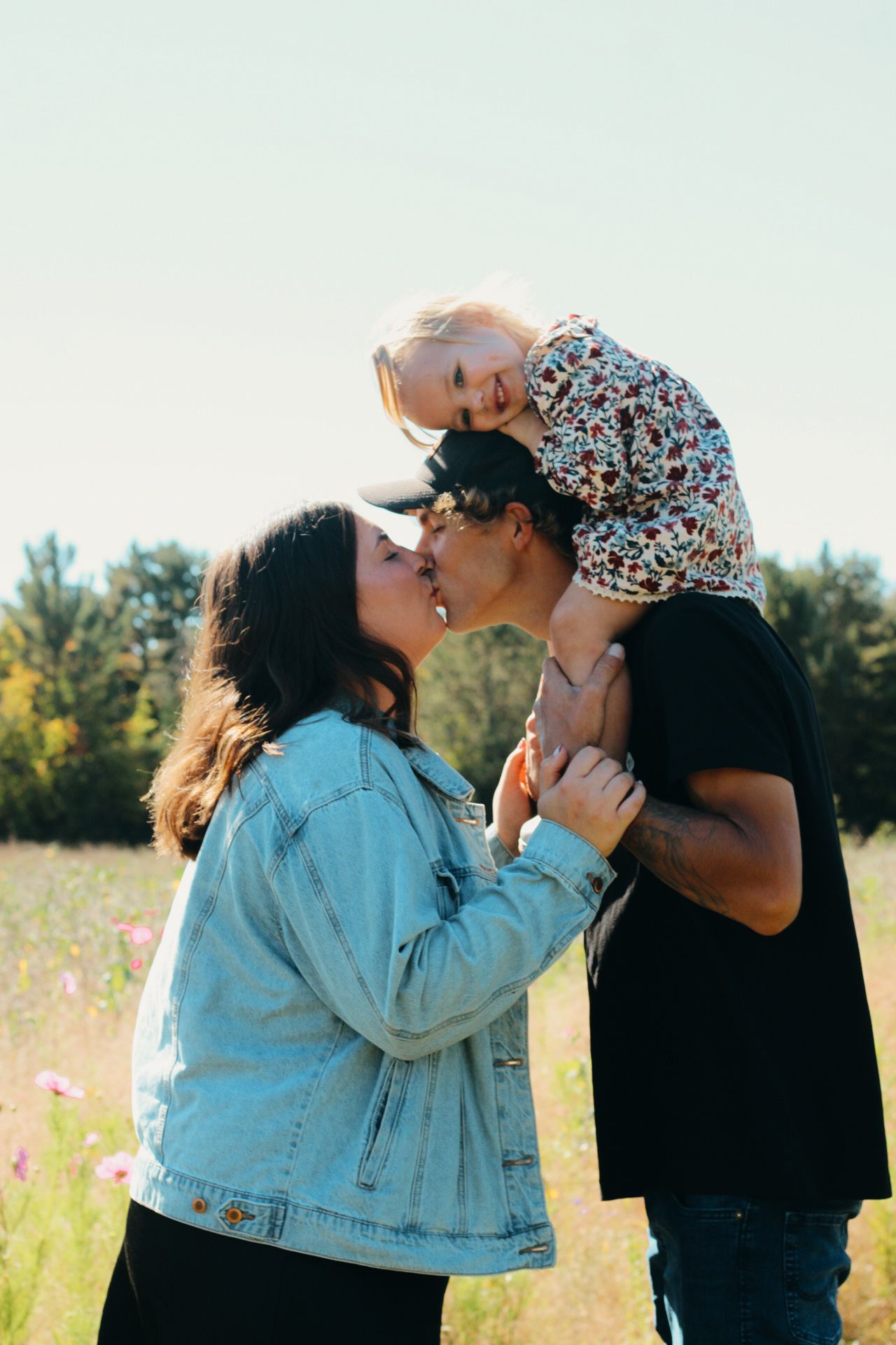 Family shares tender moment together in sunny wildflower field.