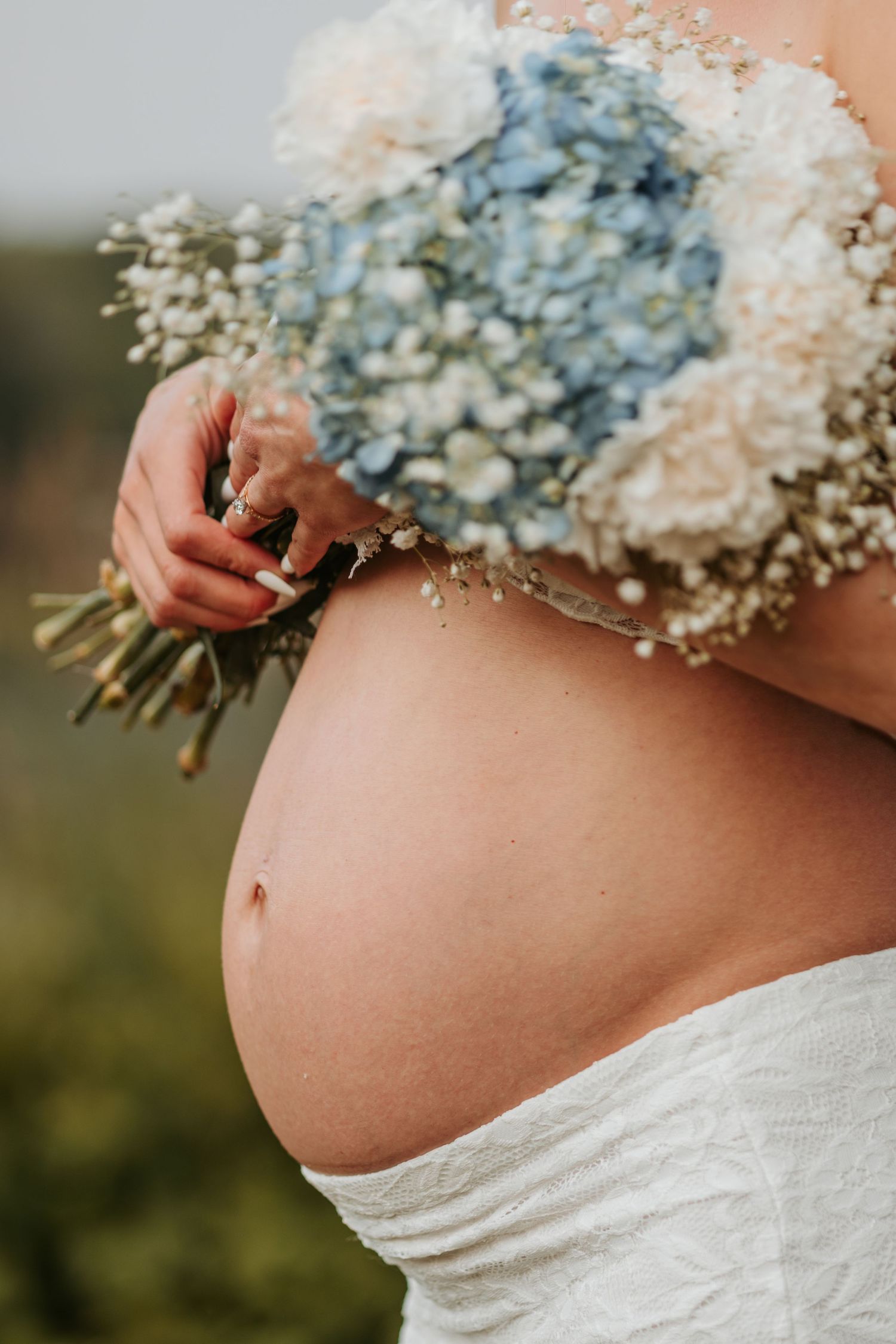 Close up of pregnant belly with delicate blue and white baby's breath flower bouquet.