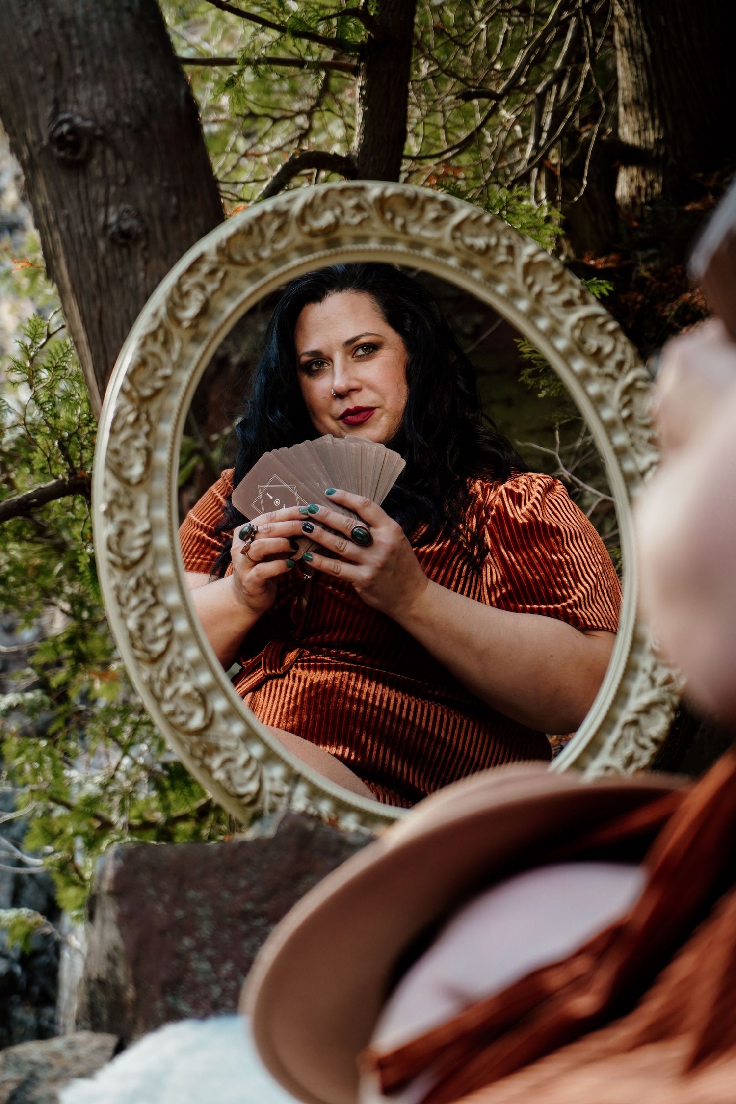 A person holds a vintage camera while sitting near a decorative ornate mirror in a garden setting.