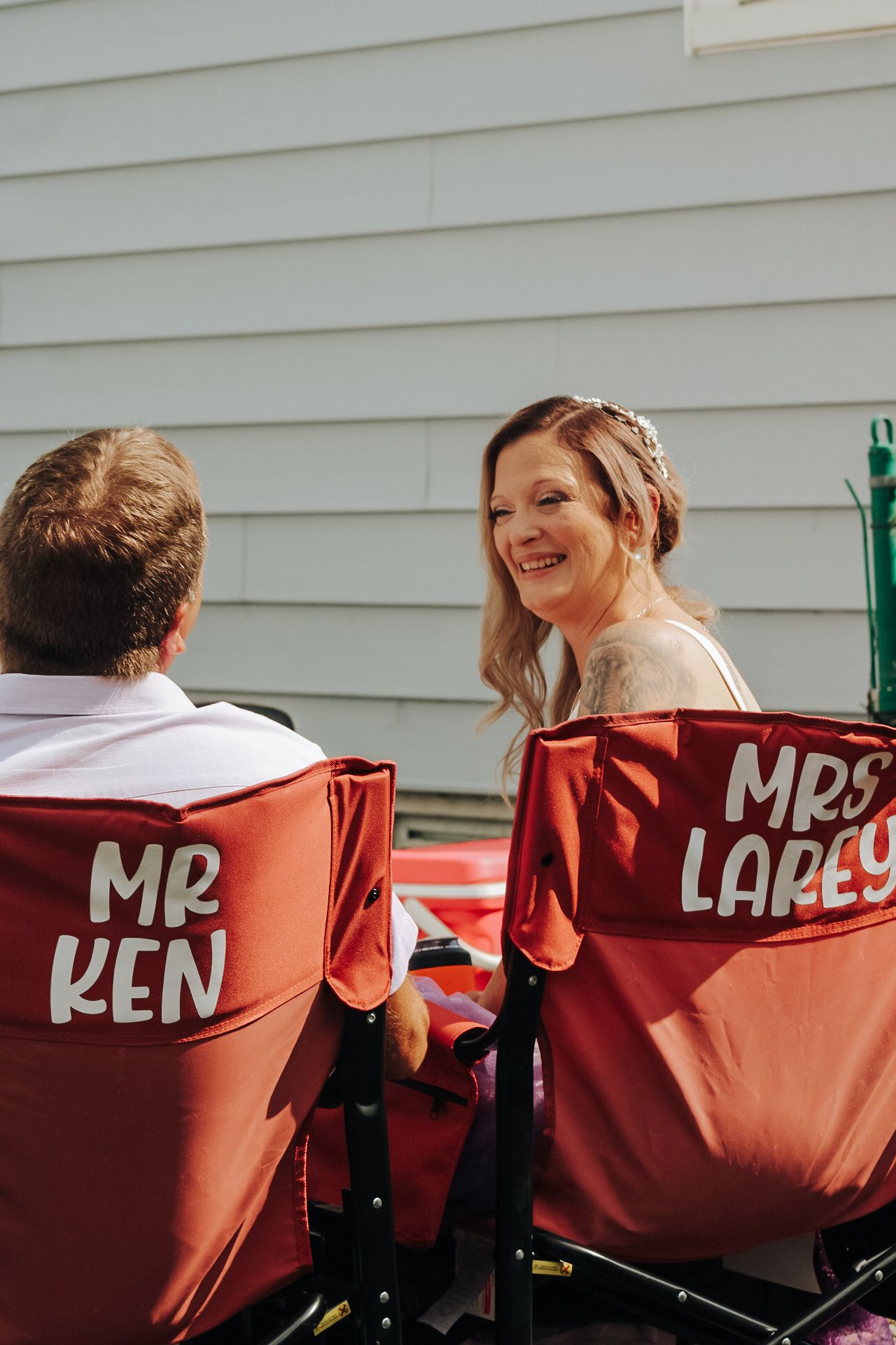 Two camping chairs with custom text 'Mr Ken' and 'Mrs Lapey' written on the red fabric backs sit side by side outdoors.