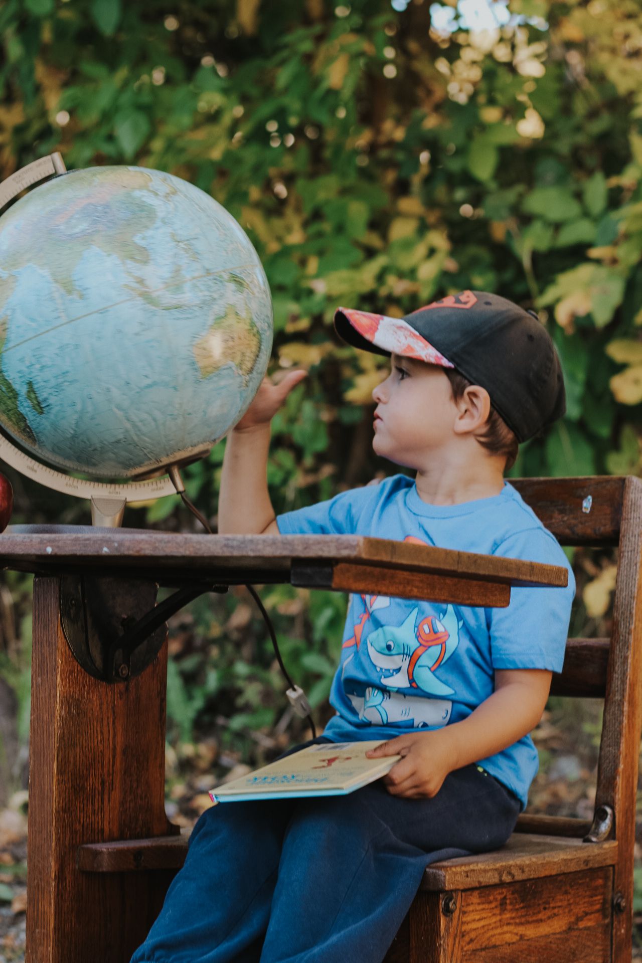 Young student in blue shirt studying world globe while sitting on wooden bench outdoors.