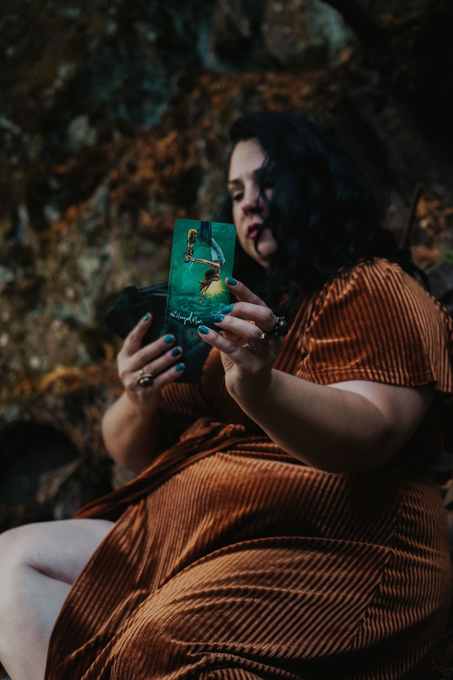Someone in a brown corduroy dress sits outdoors holding a teal phone case while looking downward.