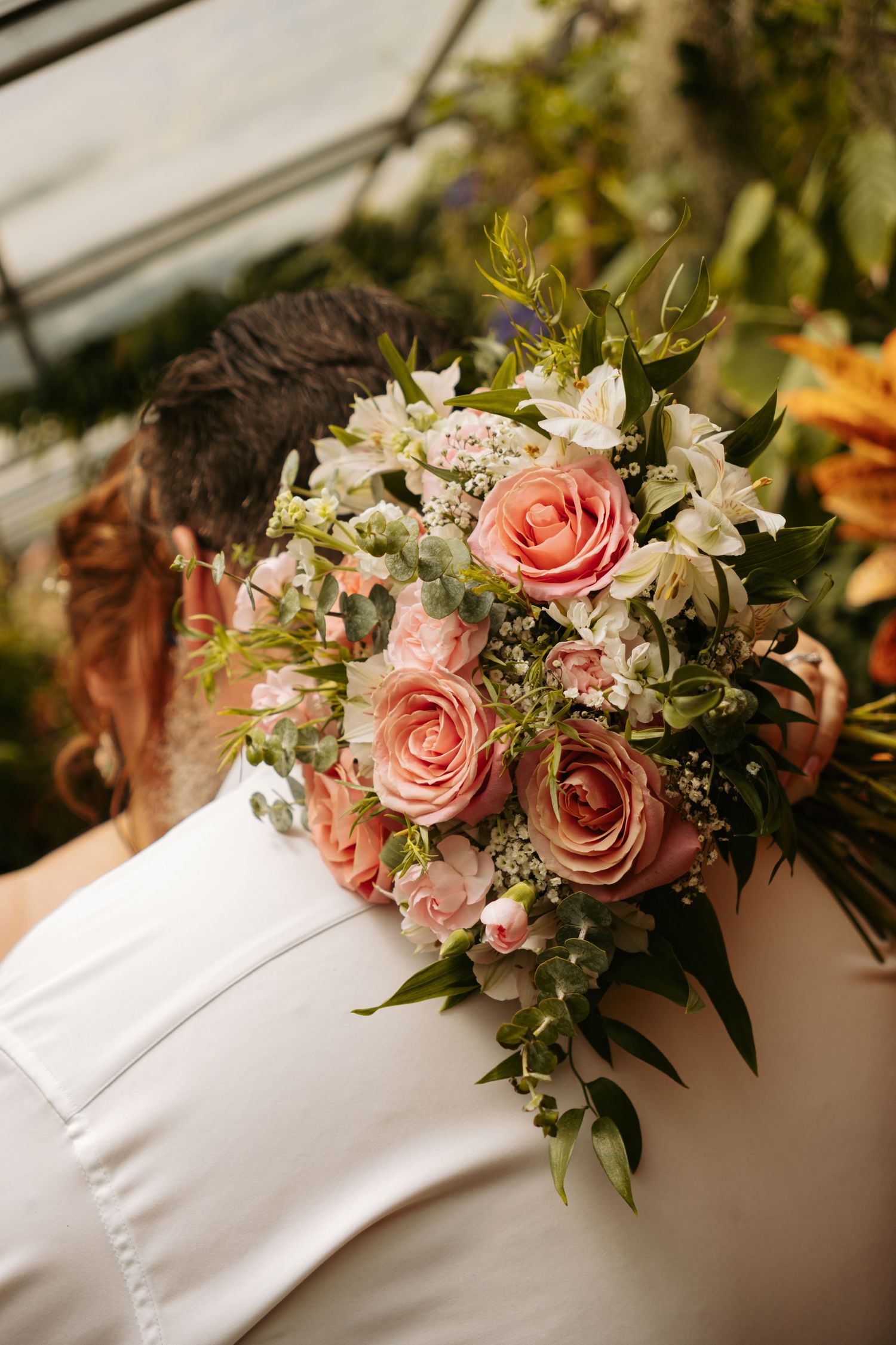 Beautiful bridal bouquet with pink roses and white flowers against a white wedding dress in soft natural light.