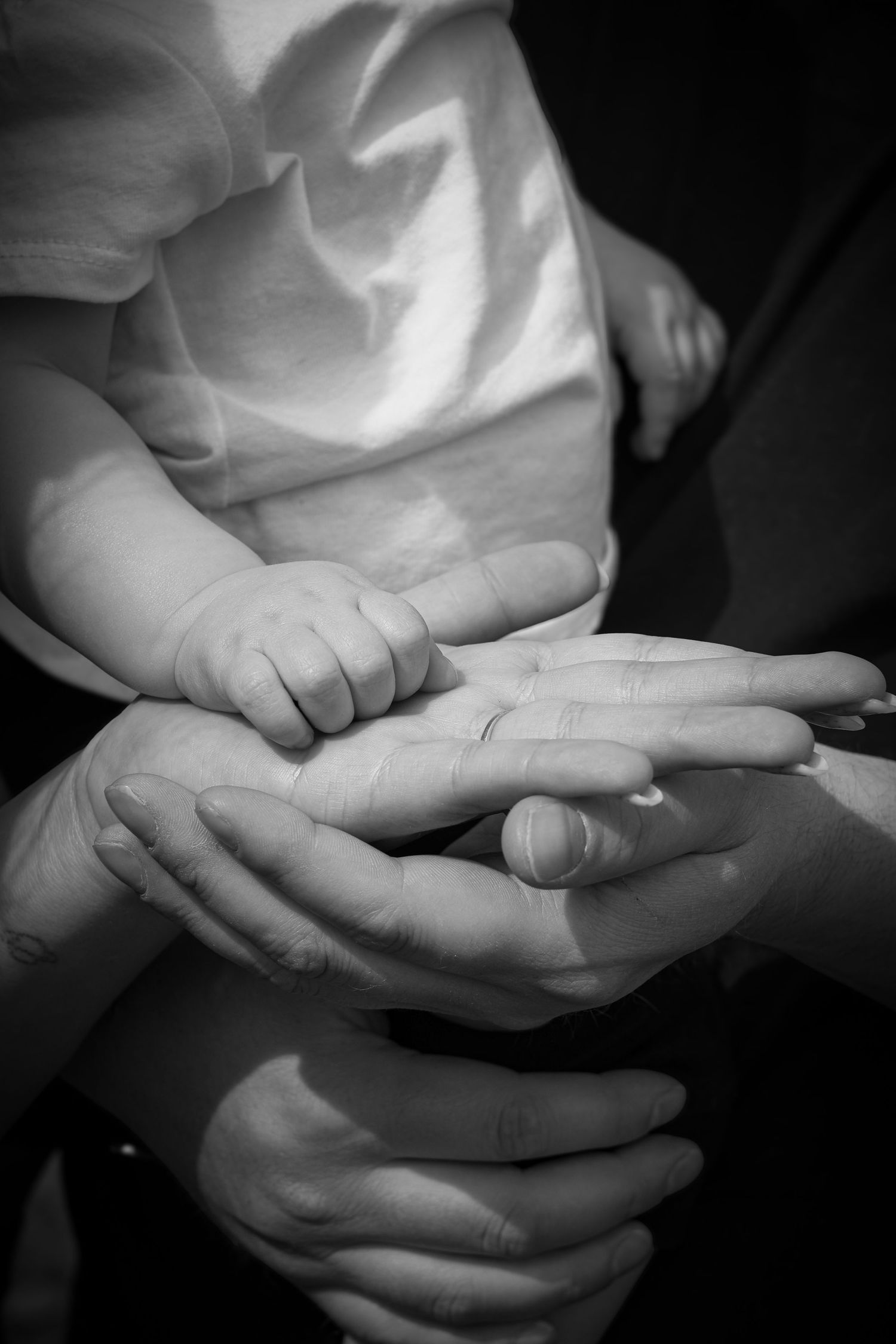 A tiny infant hand nestled within adult hands in black and white, capturing a tender moment of connection and care.