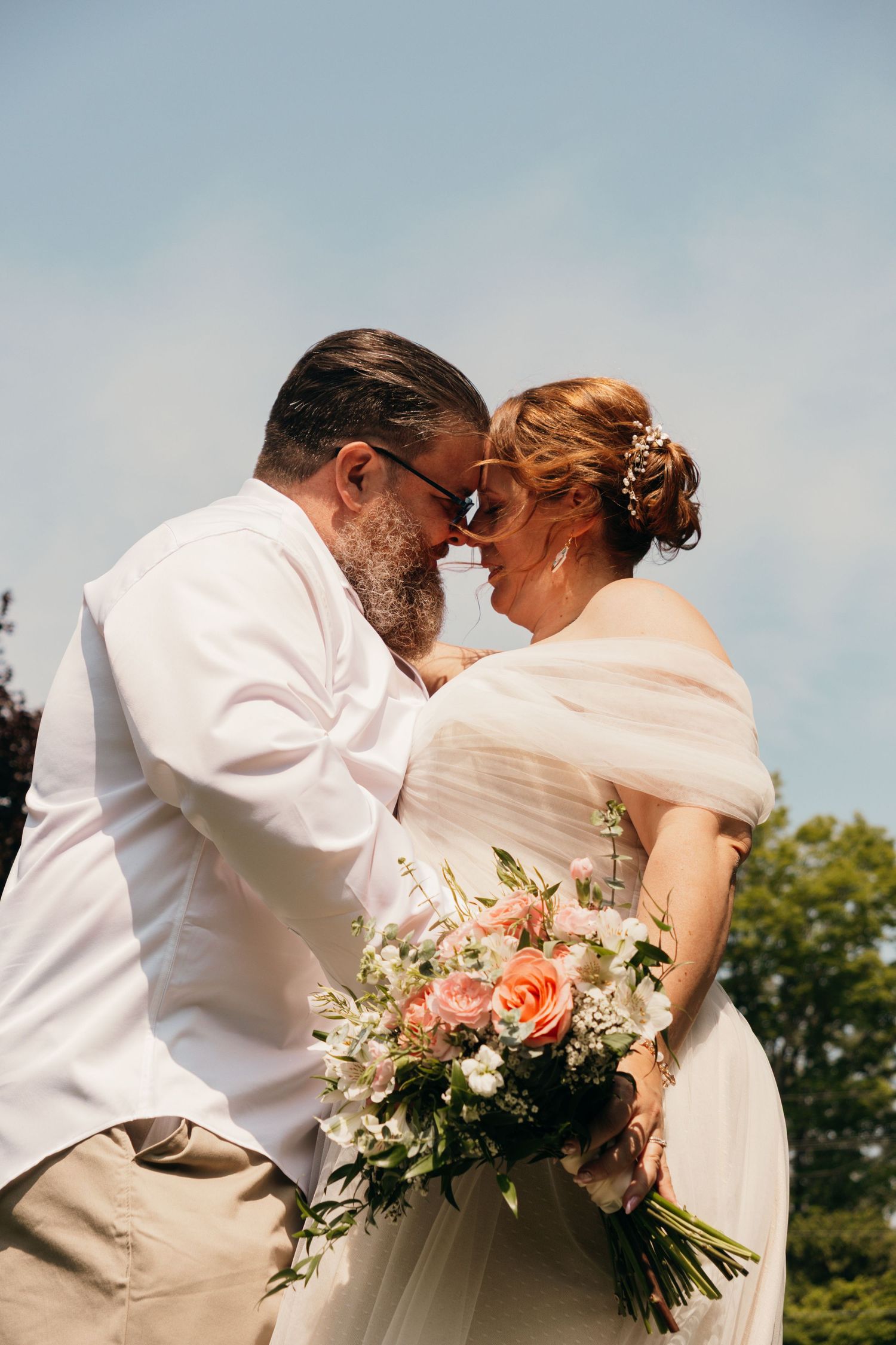 A romantic wedding couple shares sweet kisses in a series of photos against a blue sky backdrop with greenery.