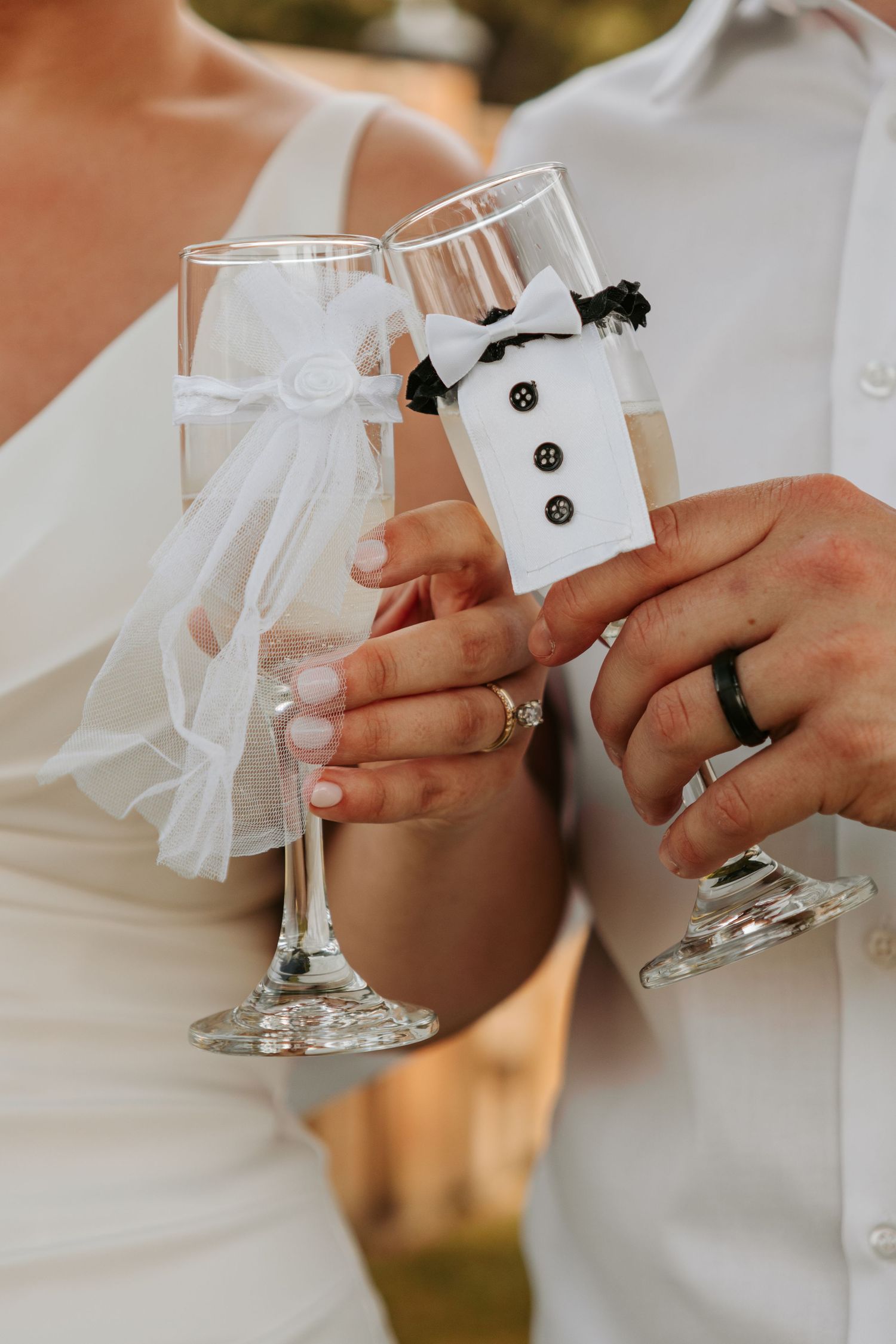 Decorated wedding champagne flutes with bride and groom designs being held by hands with matching rings.