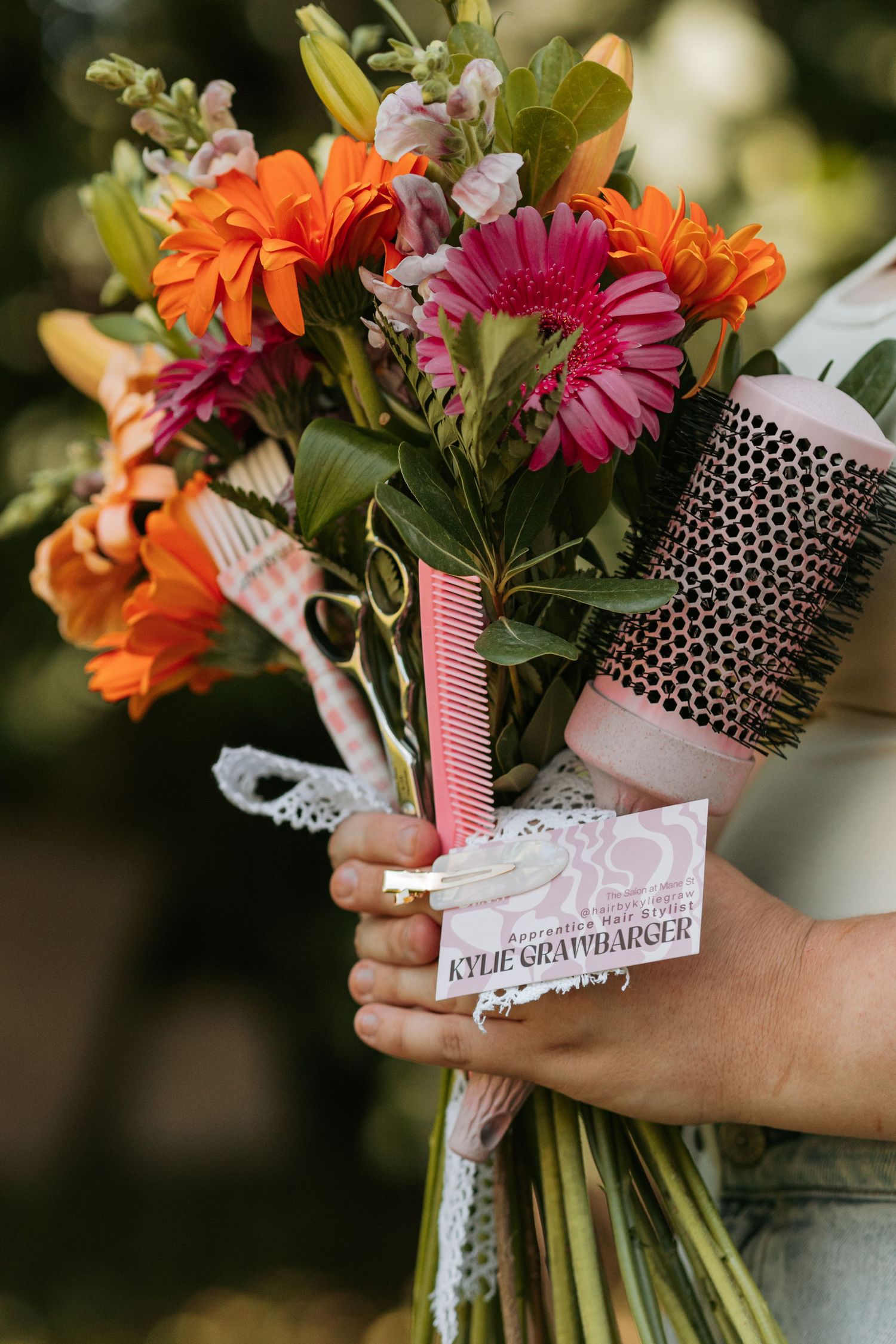 A close-up of a floral bouquet tied with polka dot ribbon shows orange and pink blooms with delicate lace accents.