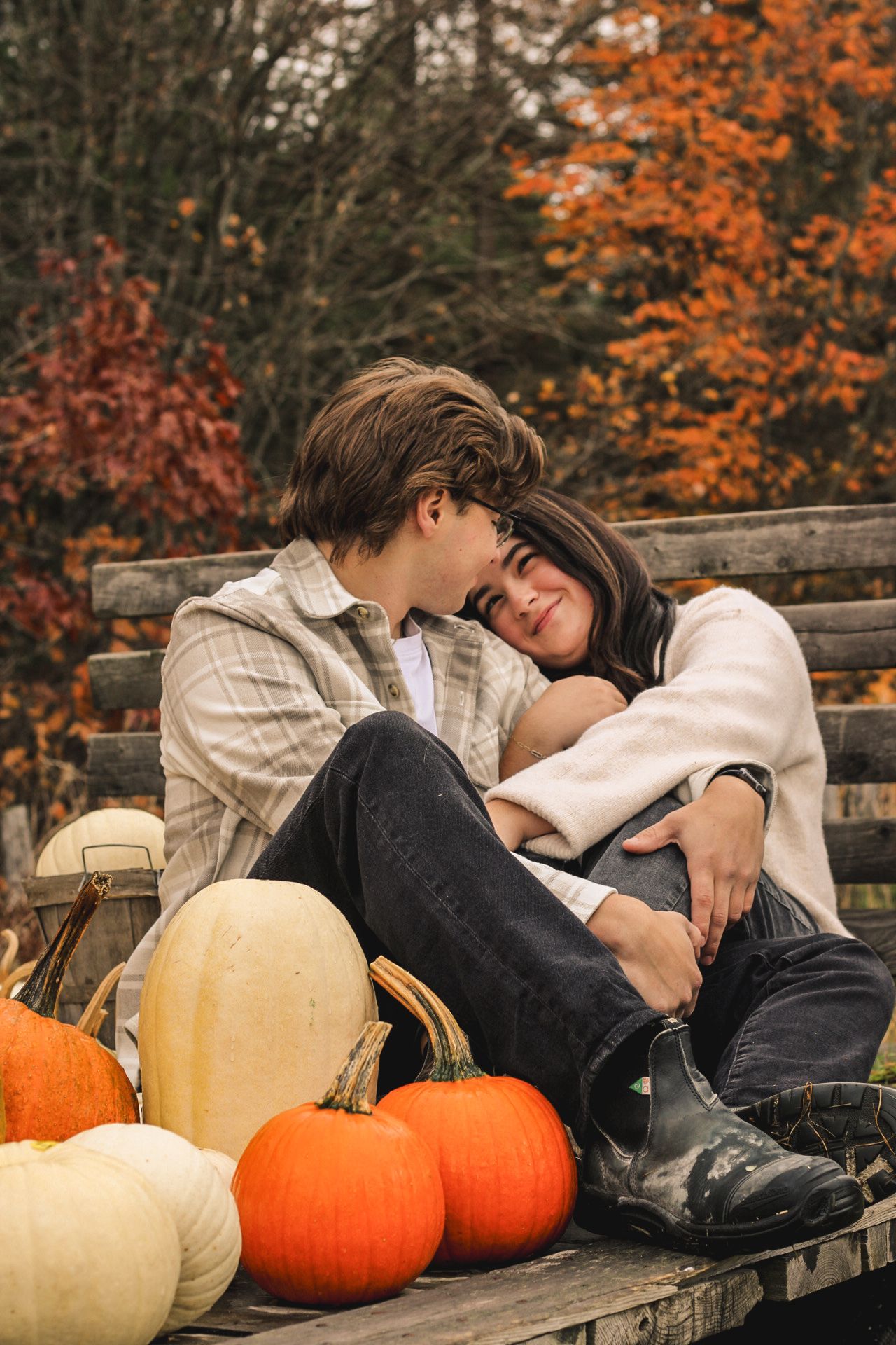 Romantic autumn scene with couple sitting on bench surrounded by orange and white pumpkins.