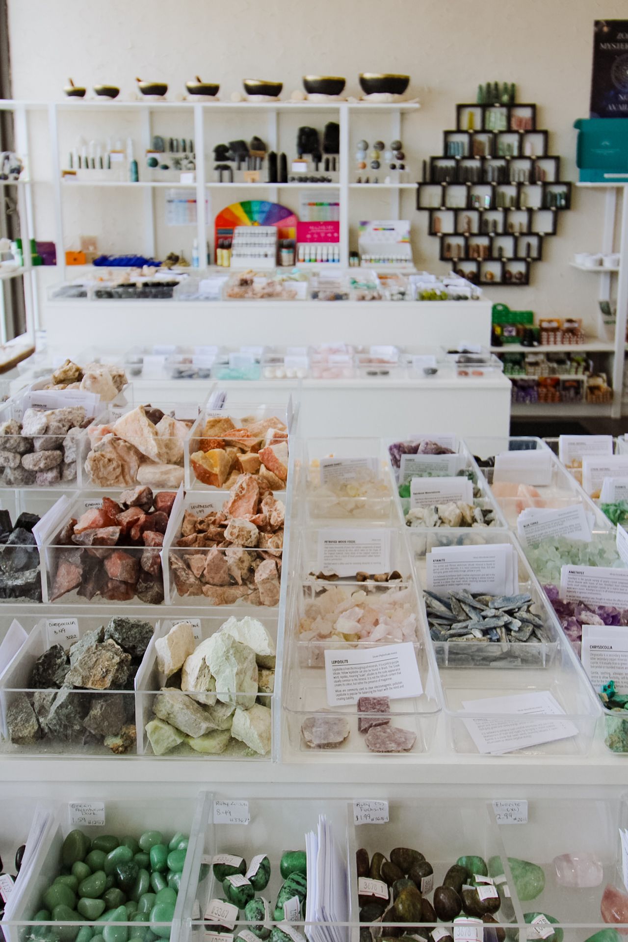 Crystal and gemstone retail display showing organized bins of colorful healing stones and minerals in white display cases.