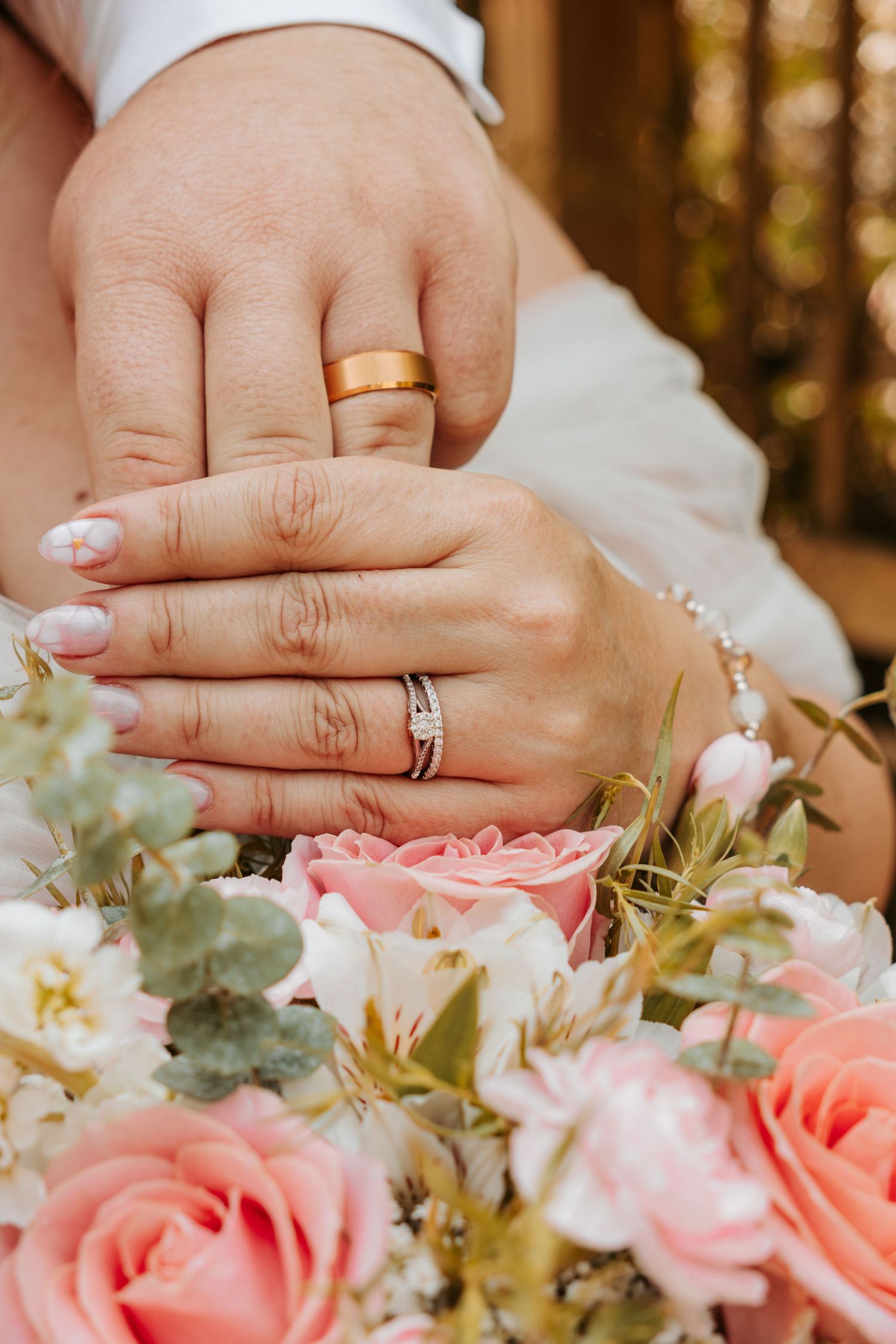Close-up collage of wedding rings on hands with pink rose wedding bouquet in the background.