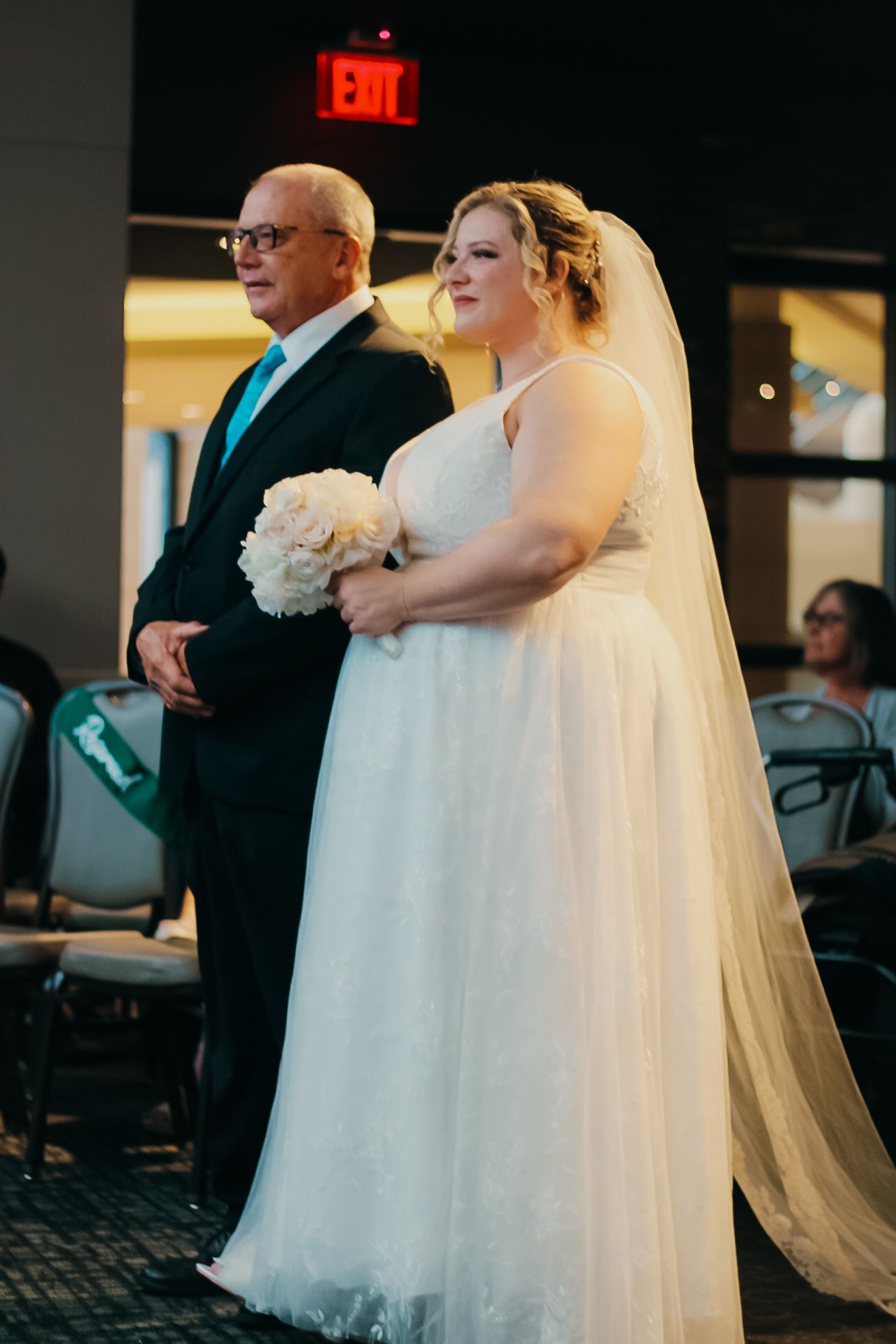 A bride holds a white bouquet while walking down the aisle in an elegant white wedding dress with flowing veil.