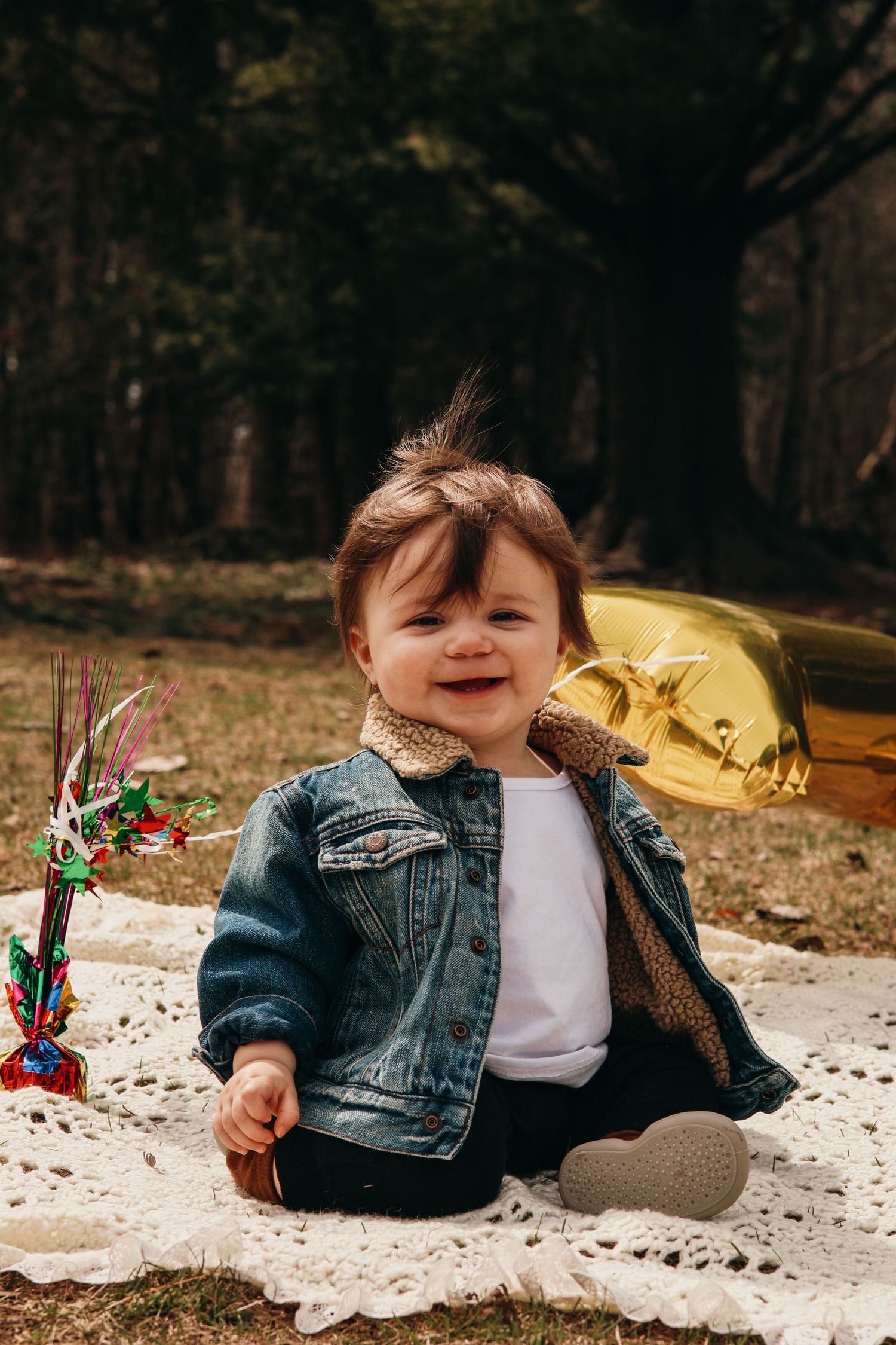 A small child laying on a blanket outside wearing denim and white clothing with a holiday lollipop.