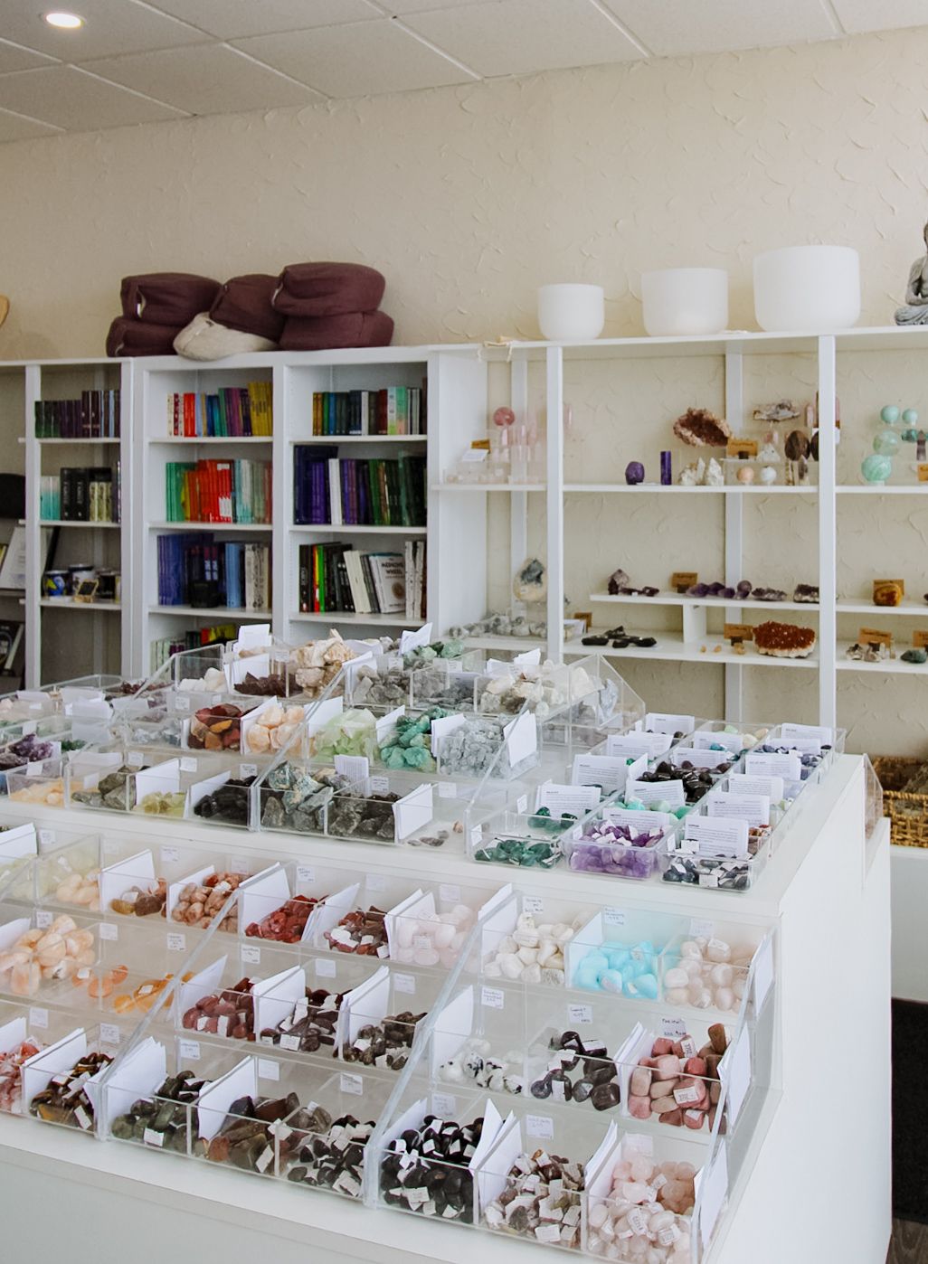 Organized crystal and mineral retail display with white shelving units showing colorful stones in clear compartments.