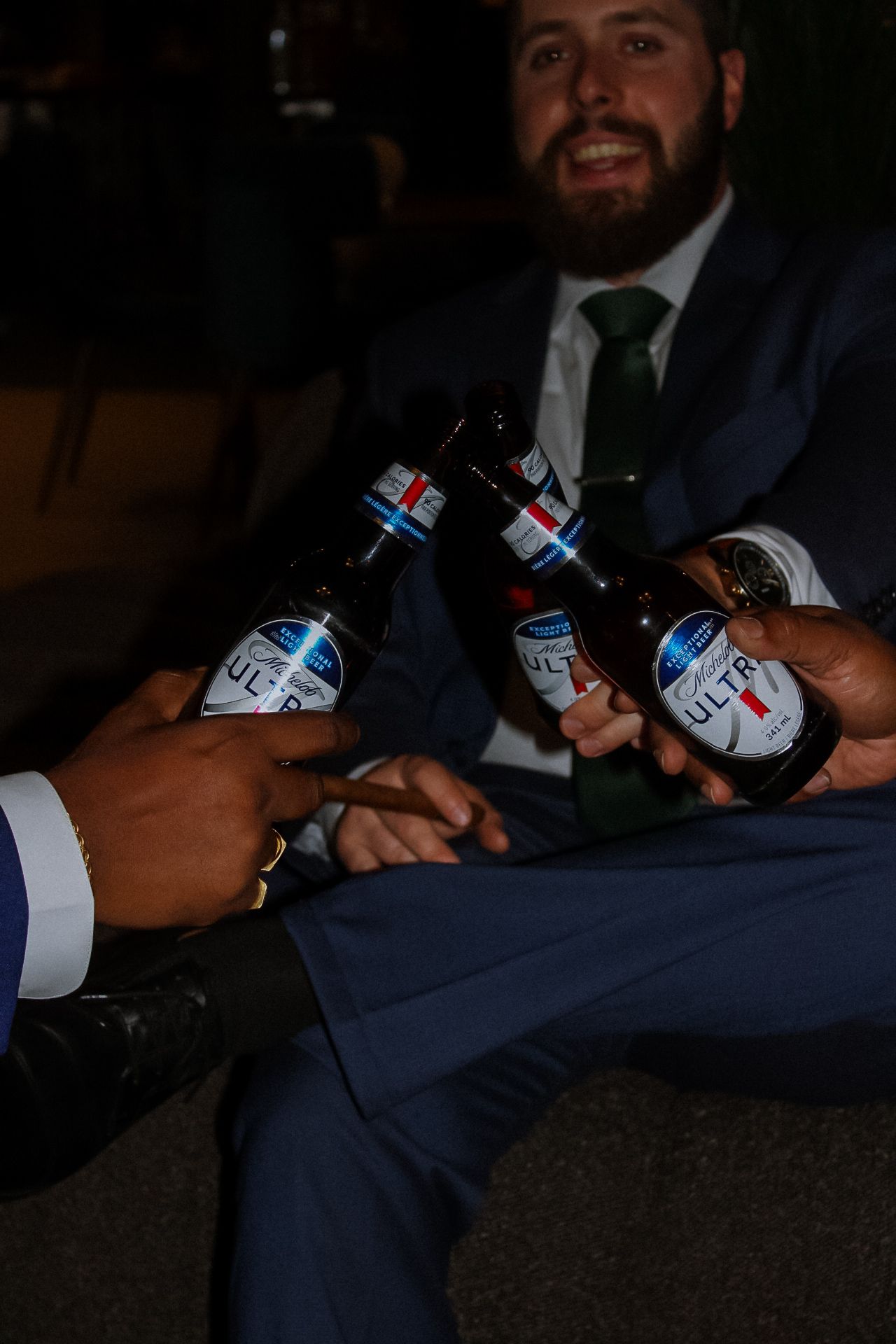 Wedding party toasts with Bud Light beer bottles in a dimly lit celebration.