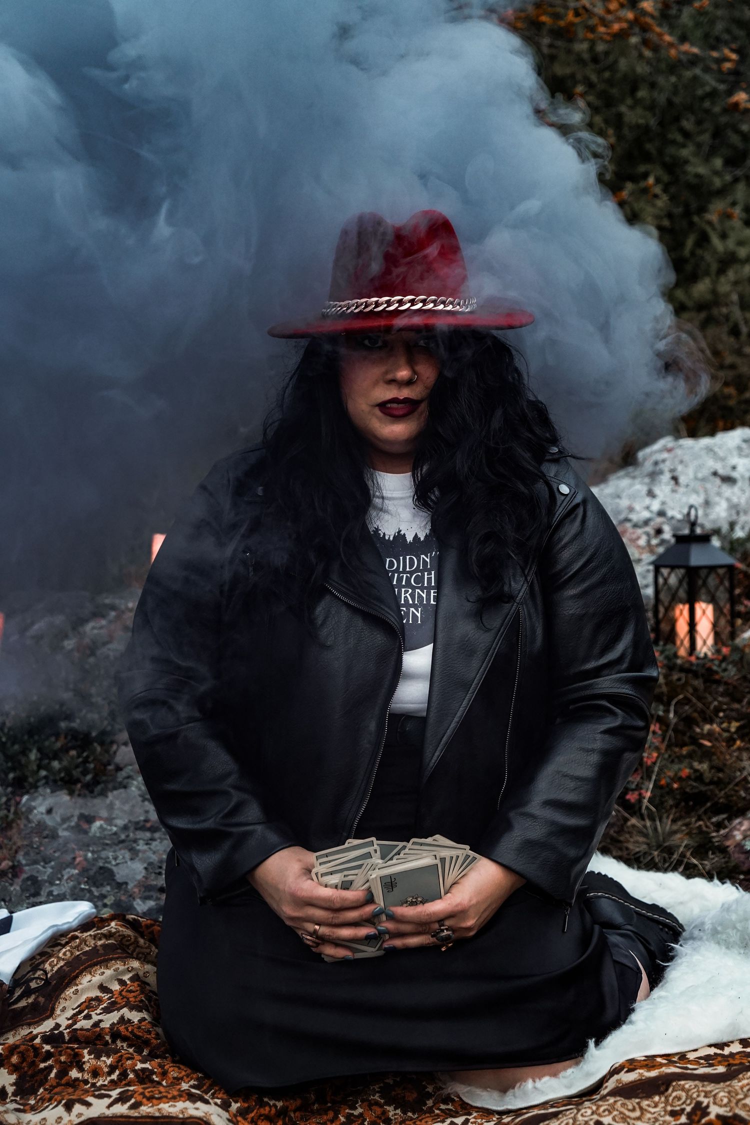 Artistic photo series showing someone in a black jacket surrounded by smoke holding a deck of cards and wearing a red hat.