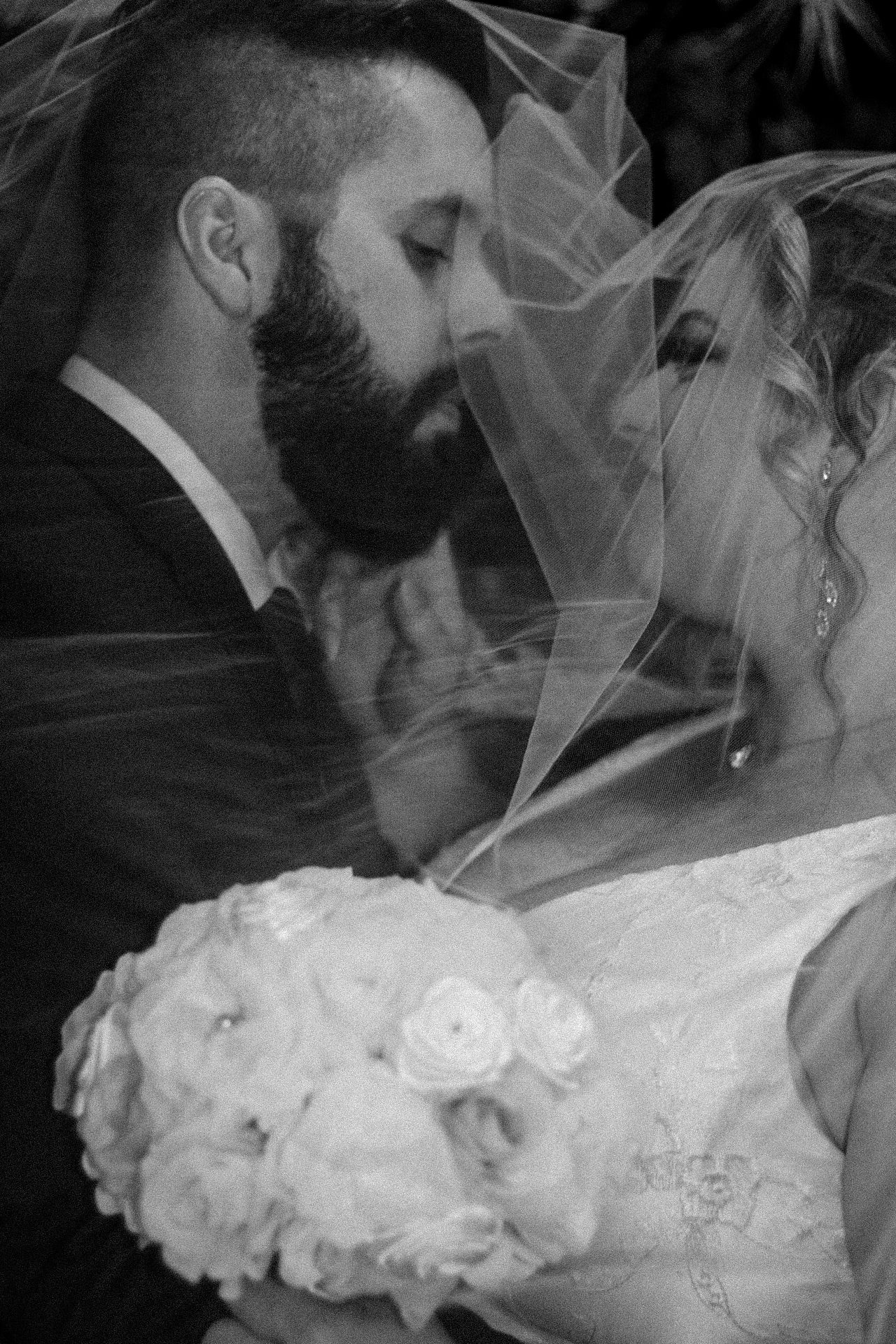 A romantic black and white wedding photo capturing an intimate moment under the bride's veil.