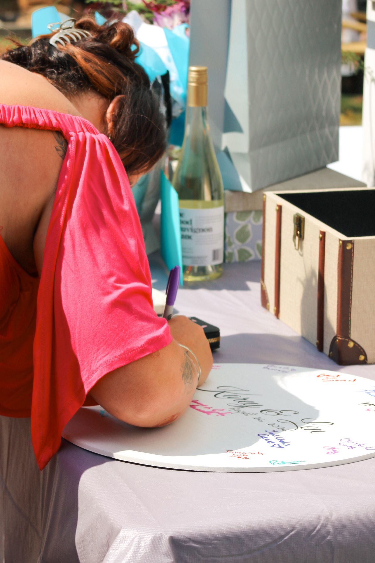 A person wearing a pink top is shown writing or drawing on a white table surface or paper.