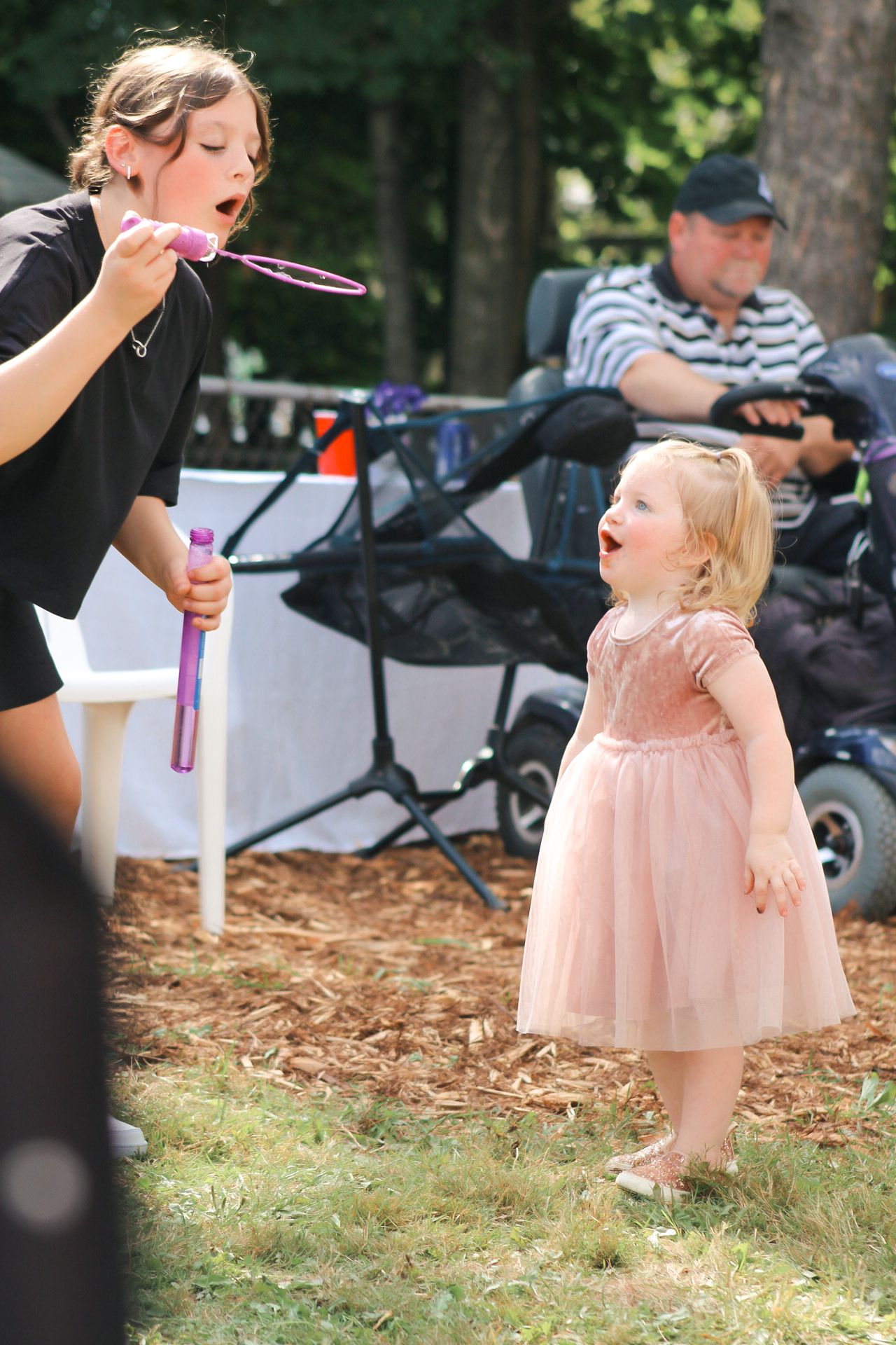 A toddler in a pink tulle dress enjoys blowing bubbles outdoors on a sunny afternoon.