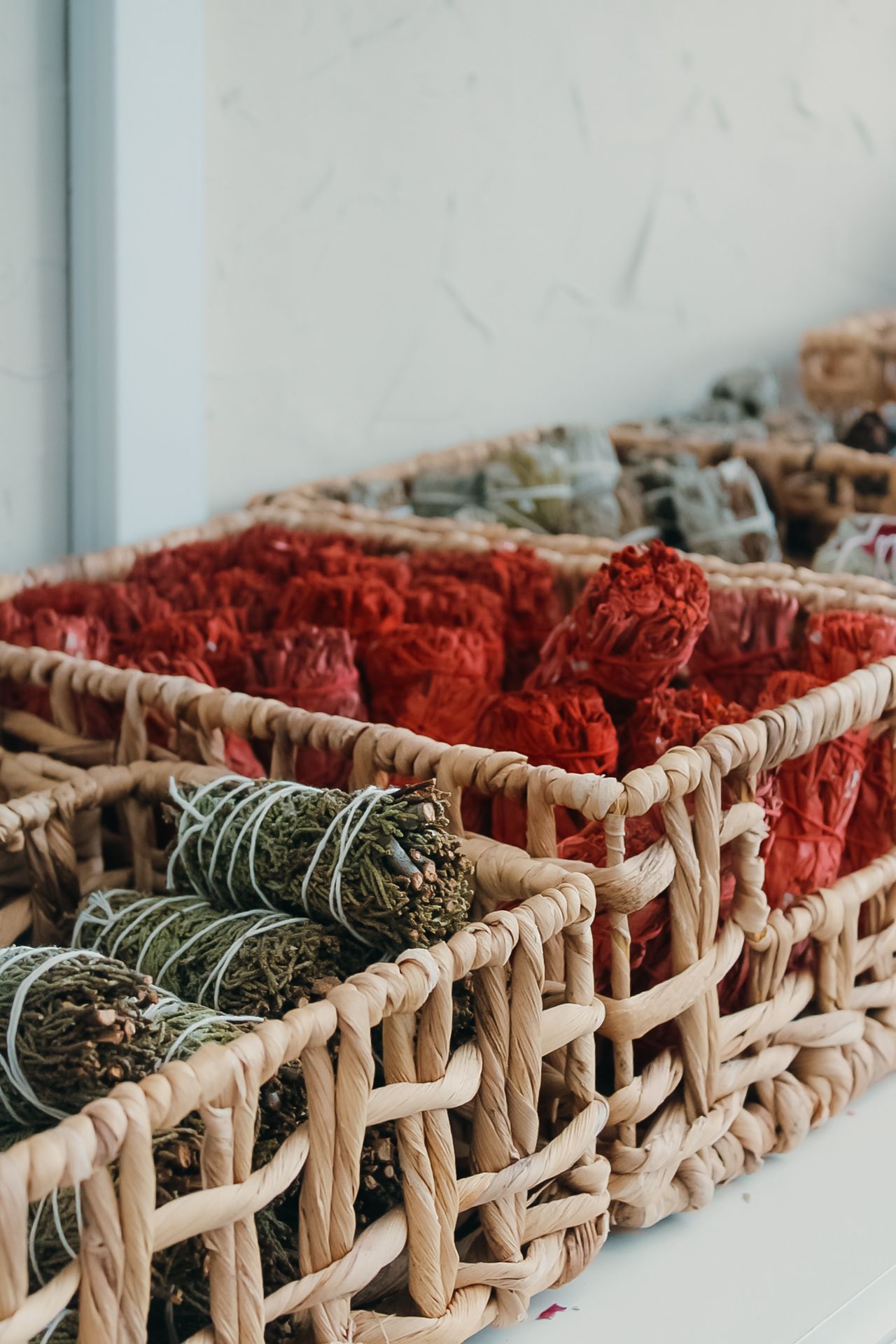 Woven basket containing red yarn and green sage smudge sticks arranged in organized compartments.