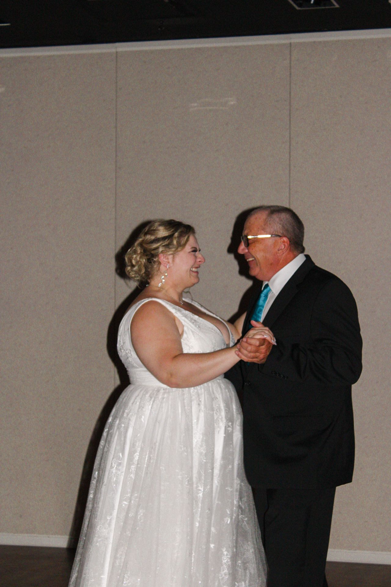 A couple dancing together at a formal event, with the woman wearing a flowing white dress and the man in dark attire.