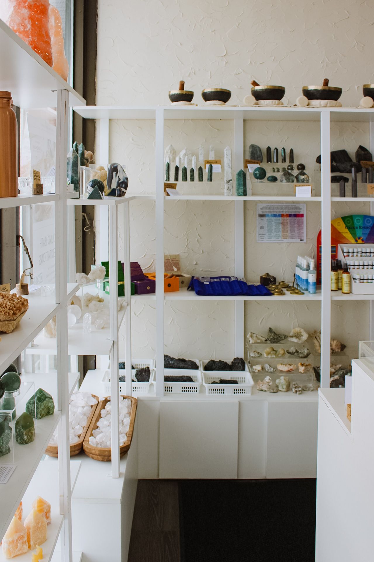 Modern white shelving system showcasing healing crystals, tools, and spiritual items in a bright retail space.