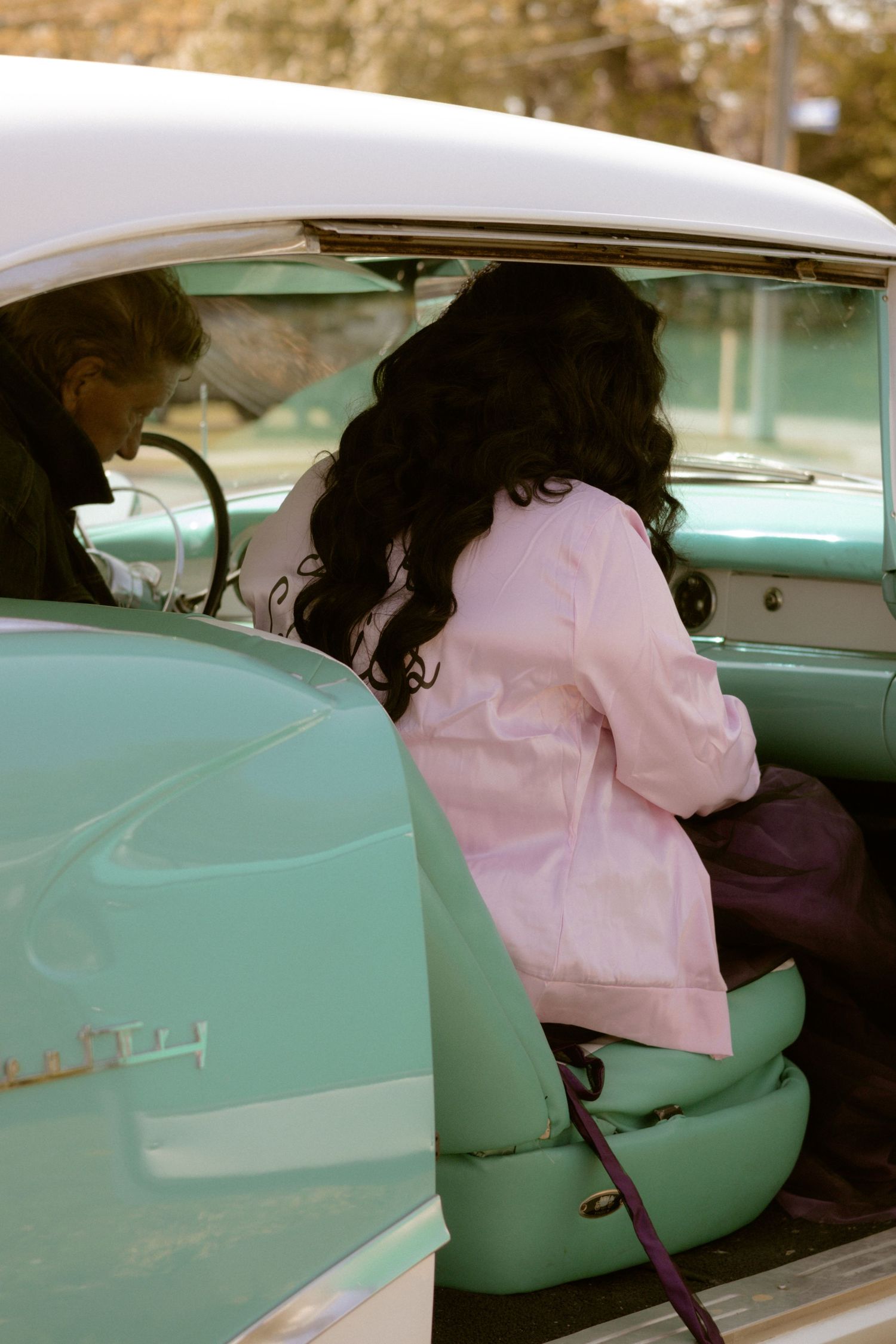 Interior view of a vintage car with mint green seats and person wearing pink jacket sitting inside.