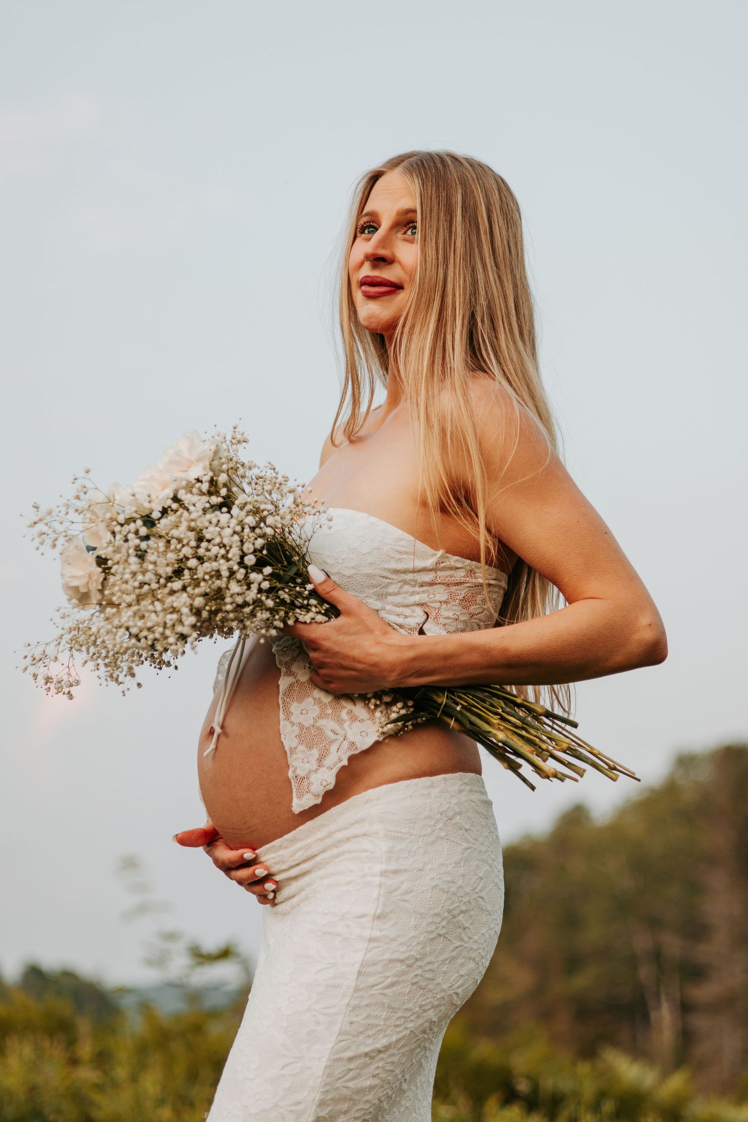 A person in a white wedding dress holds a bouquet of delicate baby's breath flowers against a natural outdoor setting.