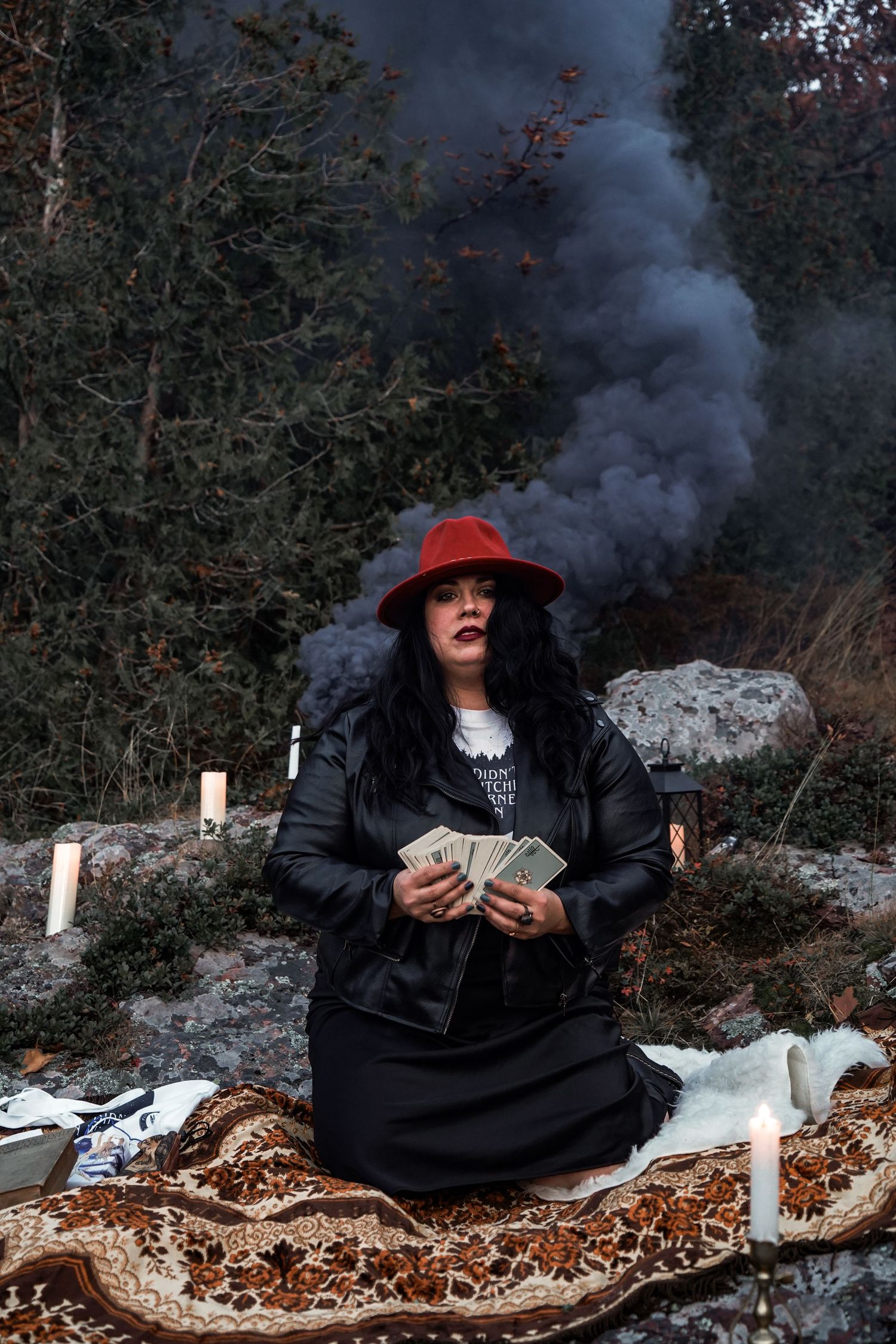 A figure in black clothing with a red hat sits on fallen leaves while releasing smoke in an artistic photo sequence.