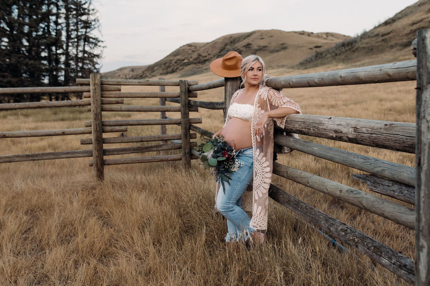 Rustic maternity photos taken near wooden fence posts in mountain landscape.