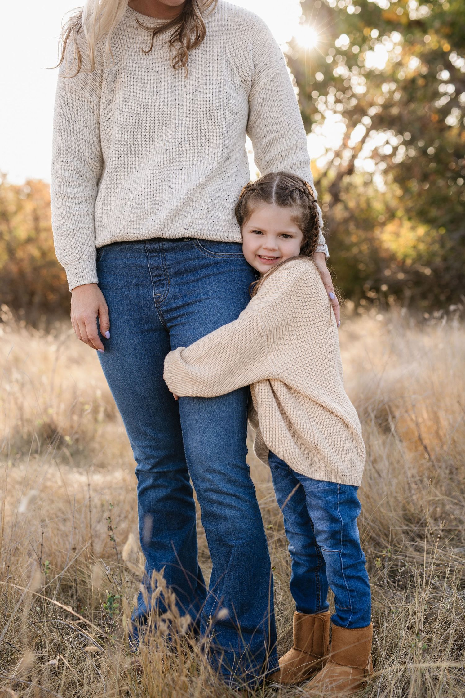 Mother and child in matching cream sweaters embracing in autumn field.