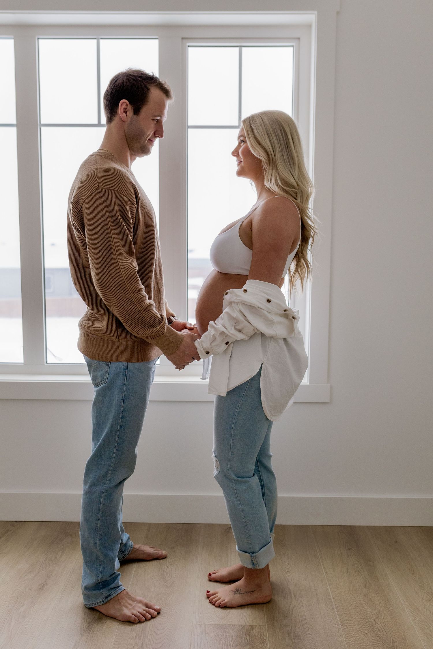 Couple in casual clothing standing together in an empty room with large windows.