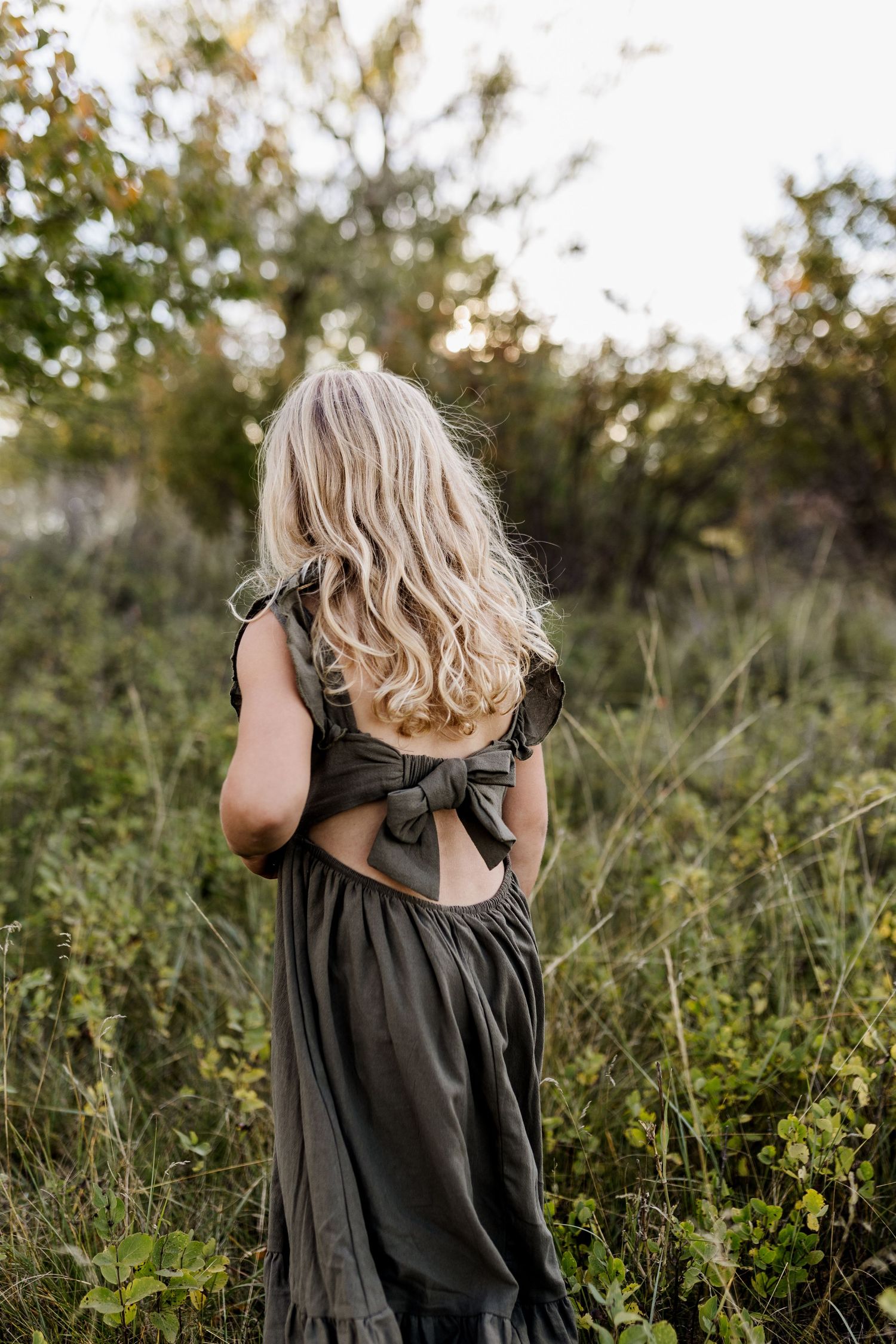 Artistic sequence showing the back view of someone in a dark dress against natural foliage.