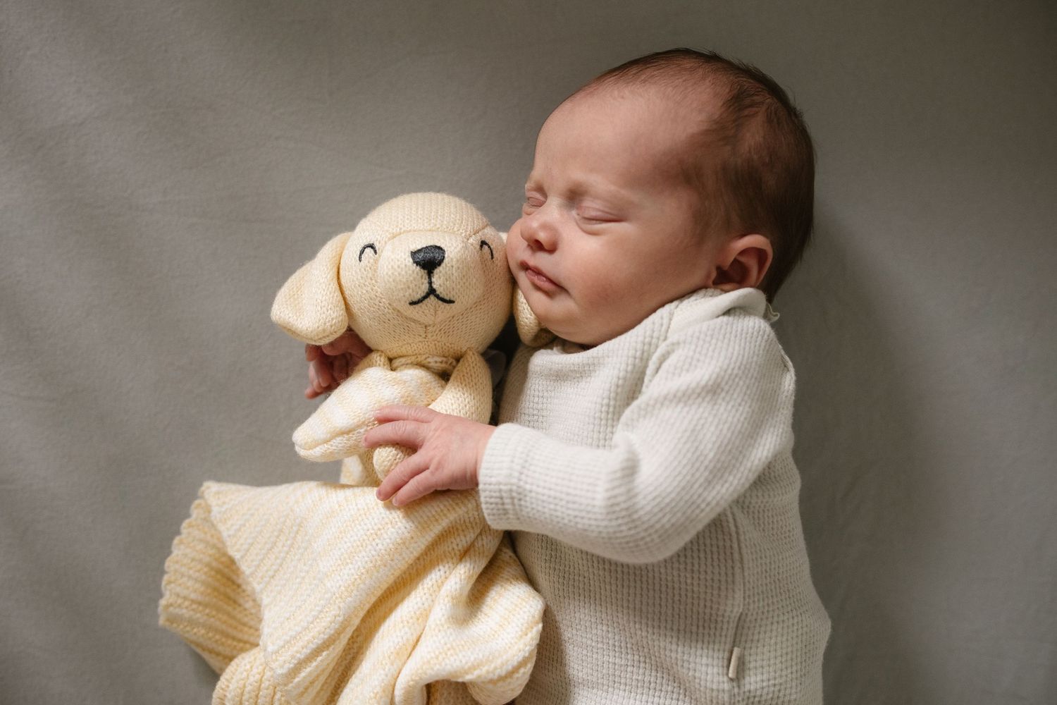 Baby in white sweater sleeping with plush teddy bear toy companion.