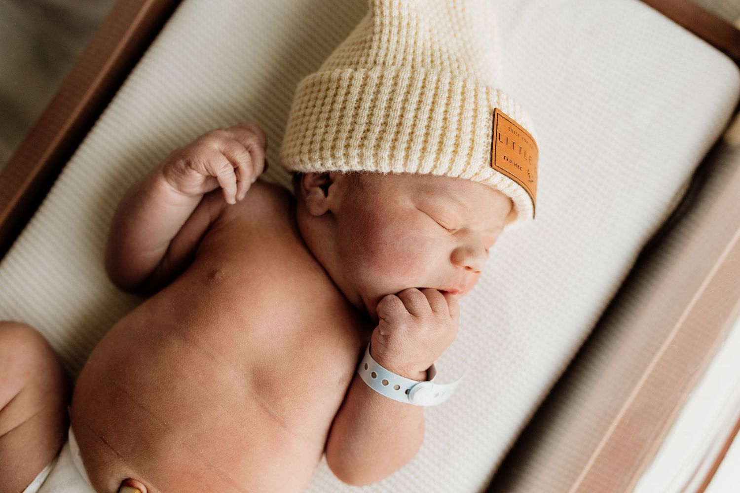 Sleeping newborn wrapped in white blanket with knit beanie hat.