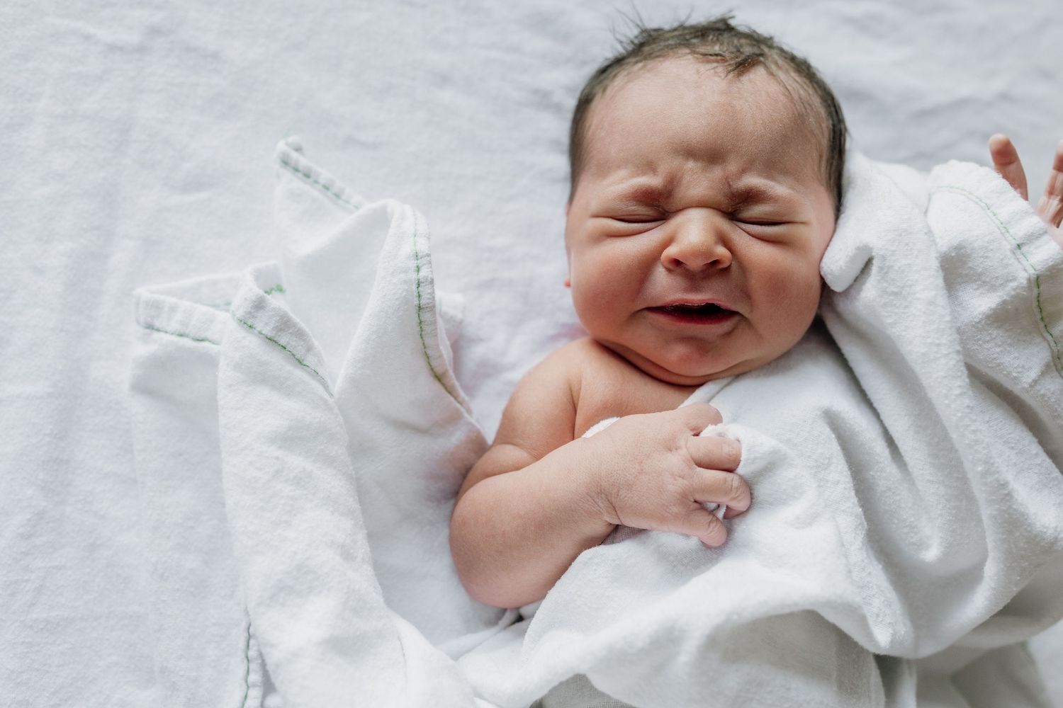 Collection of candid newborn baby expressions on white blanket.