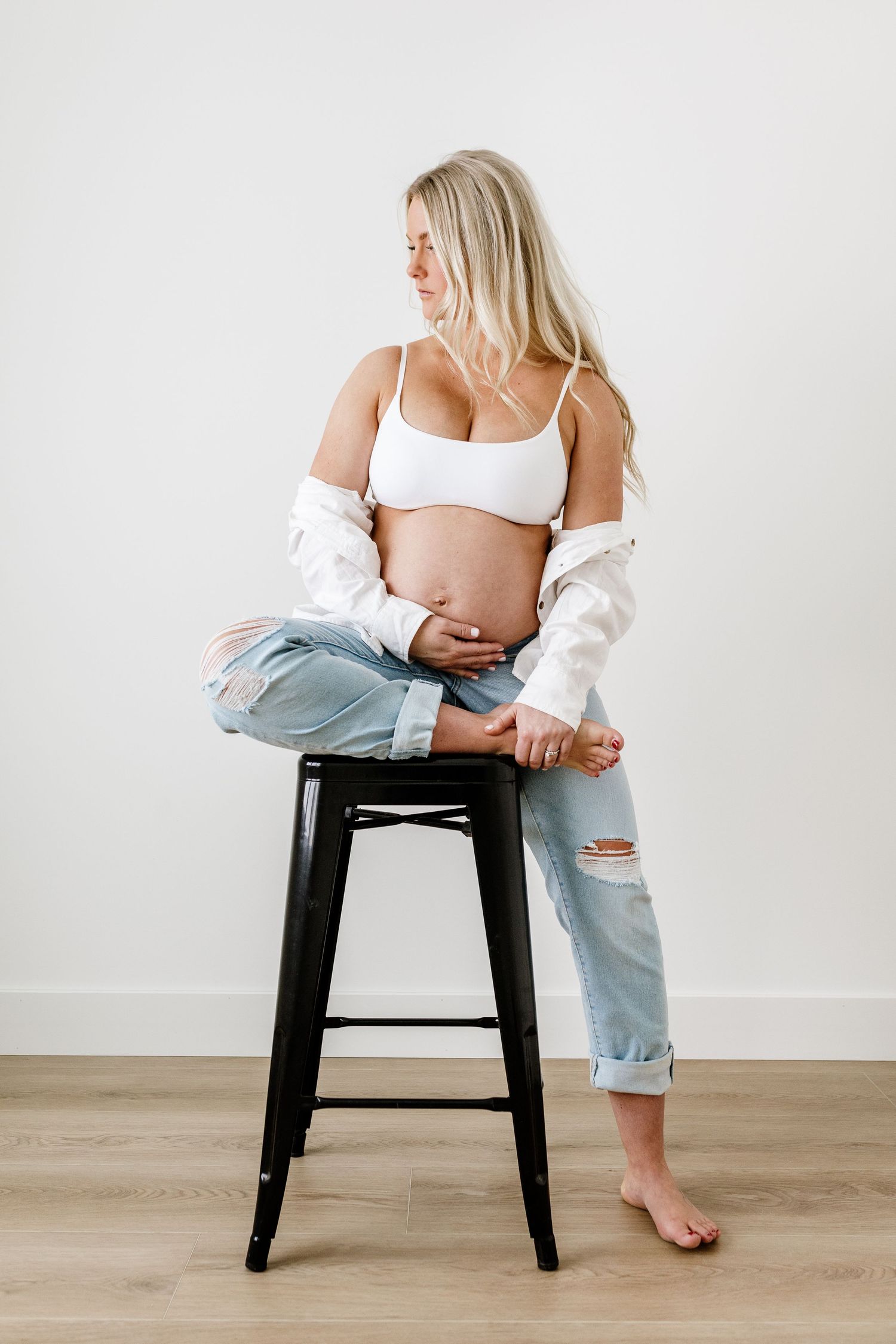 Person in casual wear sitting on black stool against white wall.