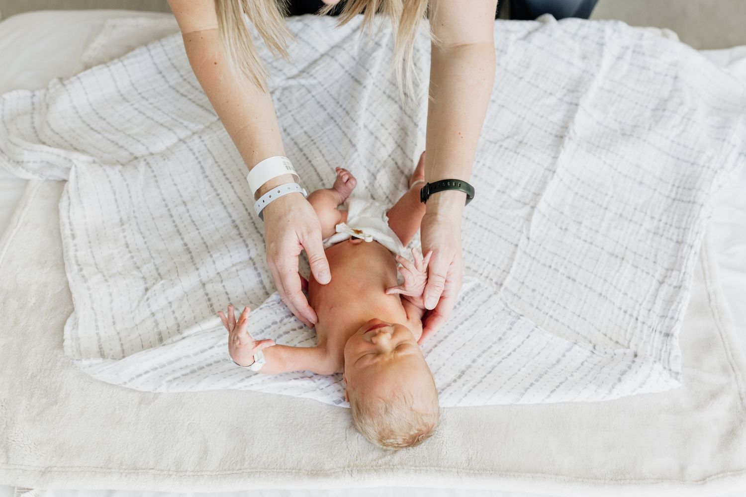 Gentle hands holding newborn baby on white textured blanket.