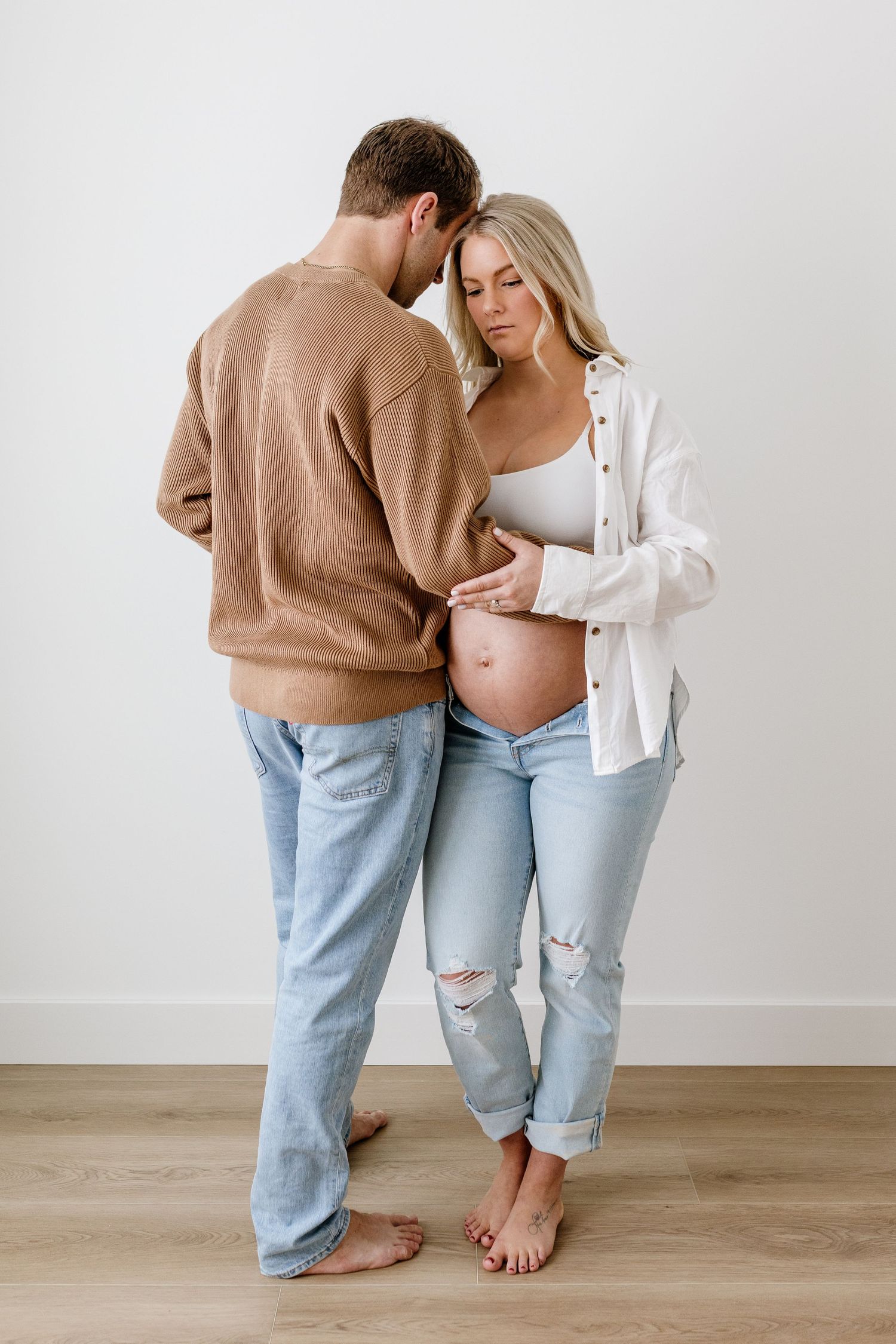 A couple in jeans and sweaters share a tender moment during their pregnancy photoshoot.