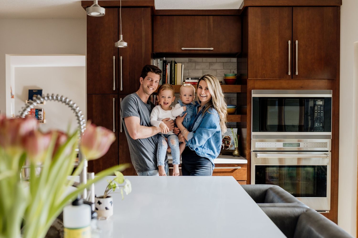 Family gathering in modern kitchen with wood cabinets and white countertops.