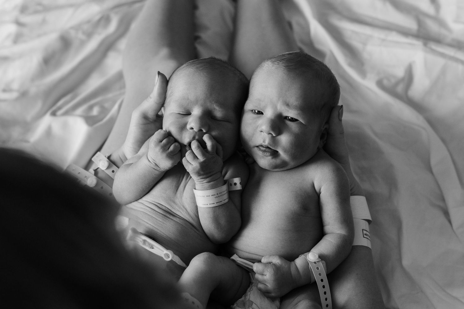 Black and white photo of two babies lying together on soft bedding.