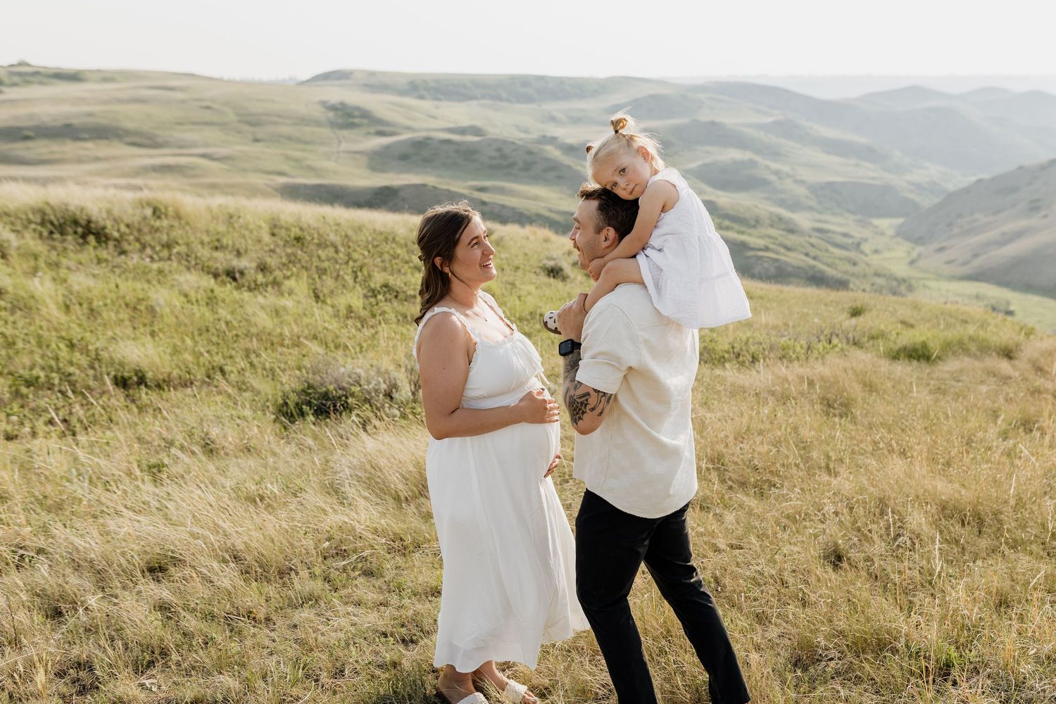 Couple embracing on a scenic hilltop with rolling green mountains in the background.