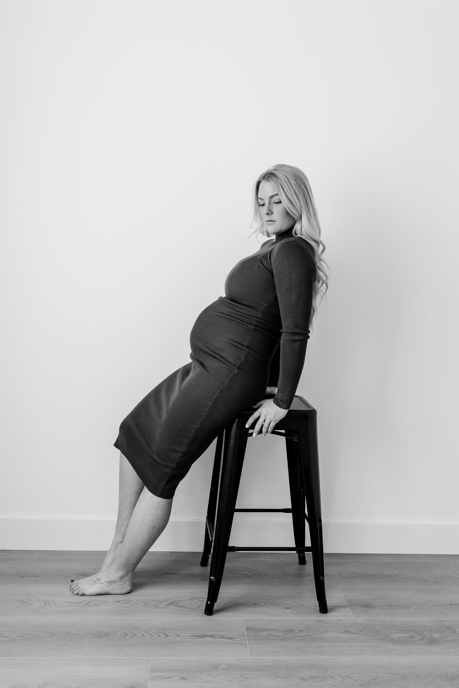Artistic black and white maternity poses on chair against white backdrop.