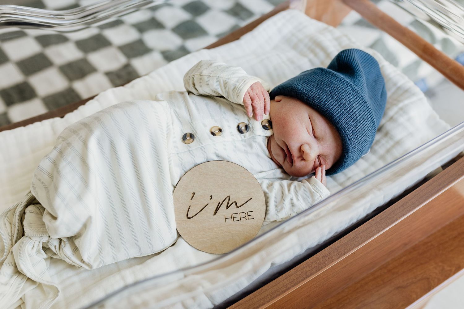Newborn baby sleeping peacefully in a wooden hospital bassinet with white bedding.