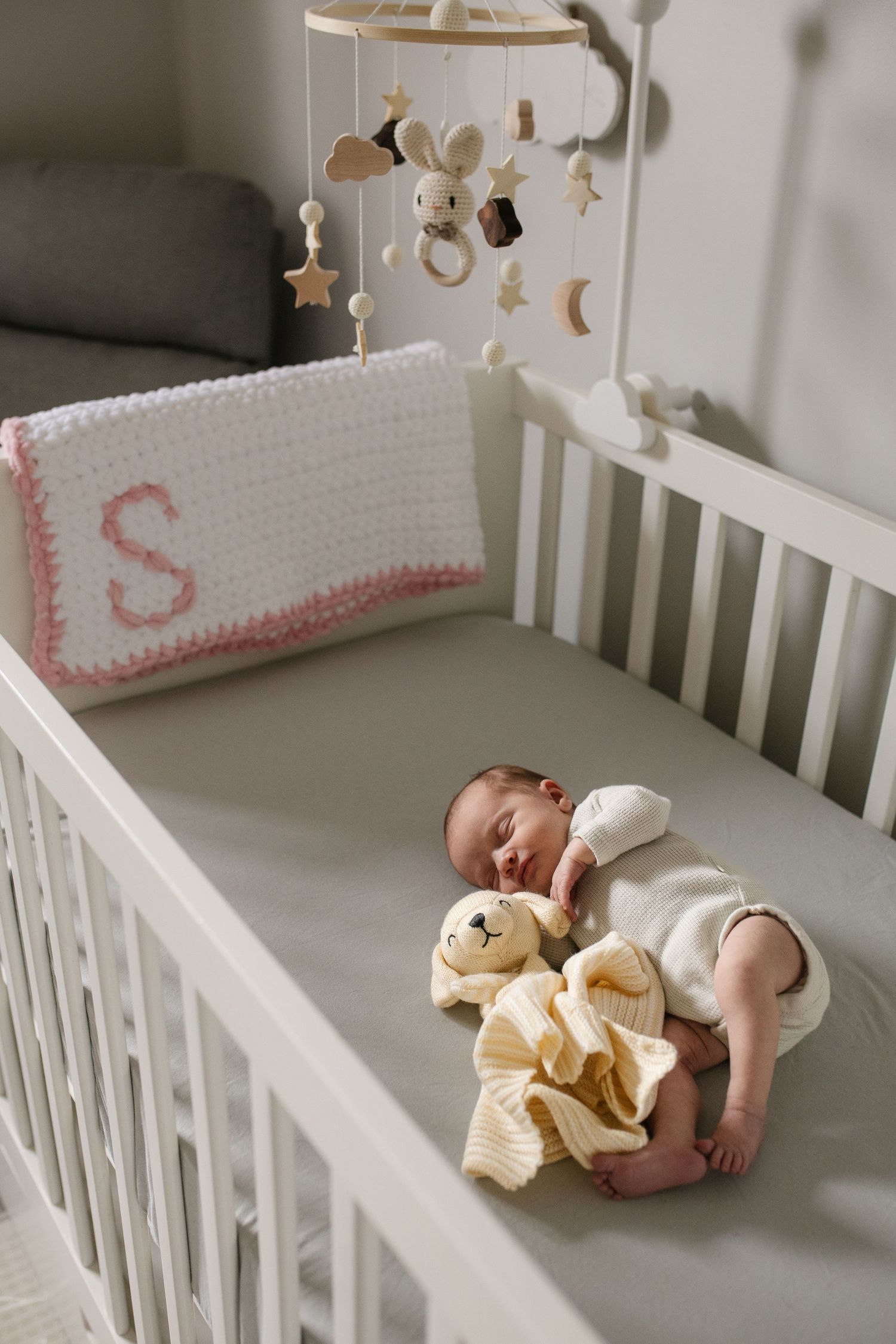 Baby sleeping peacefully in white crib with mobile and decorative cushions.