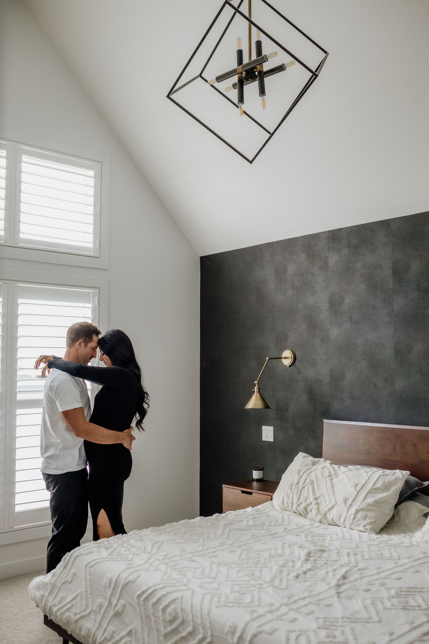 Couple playfully interacting on white bed in modern bedroom with gray accent wall.