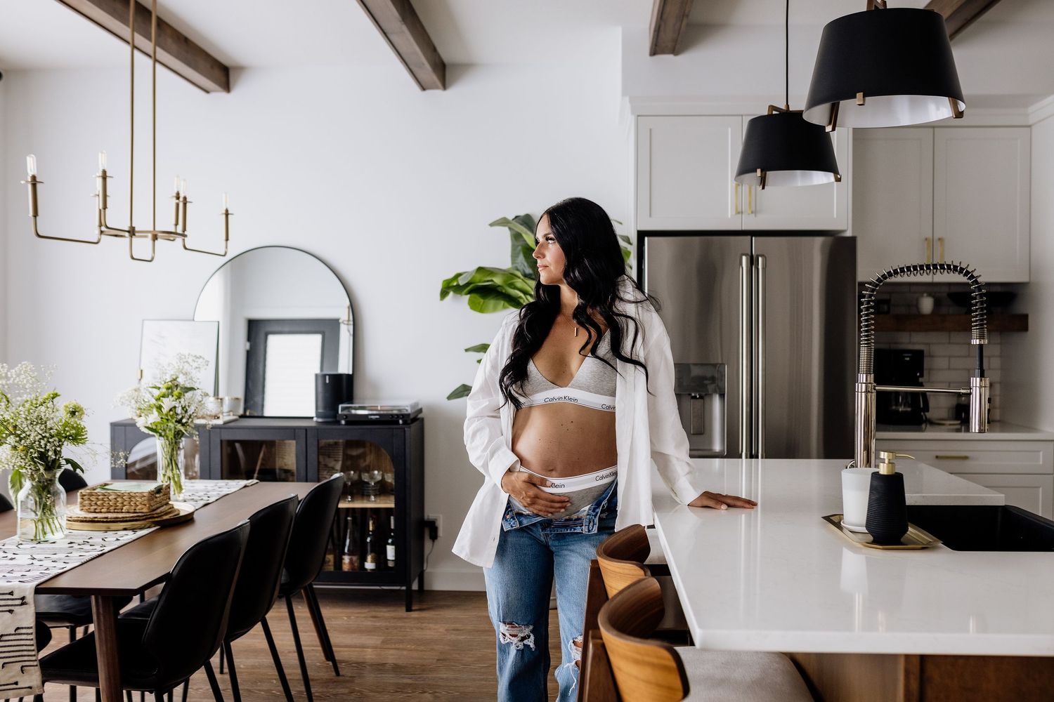Modern minimalist kitchen interior with white cabinets, black pendant lights and exposed wooden ceiling beams.