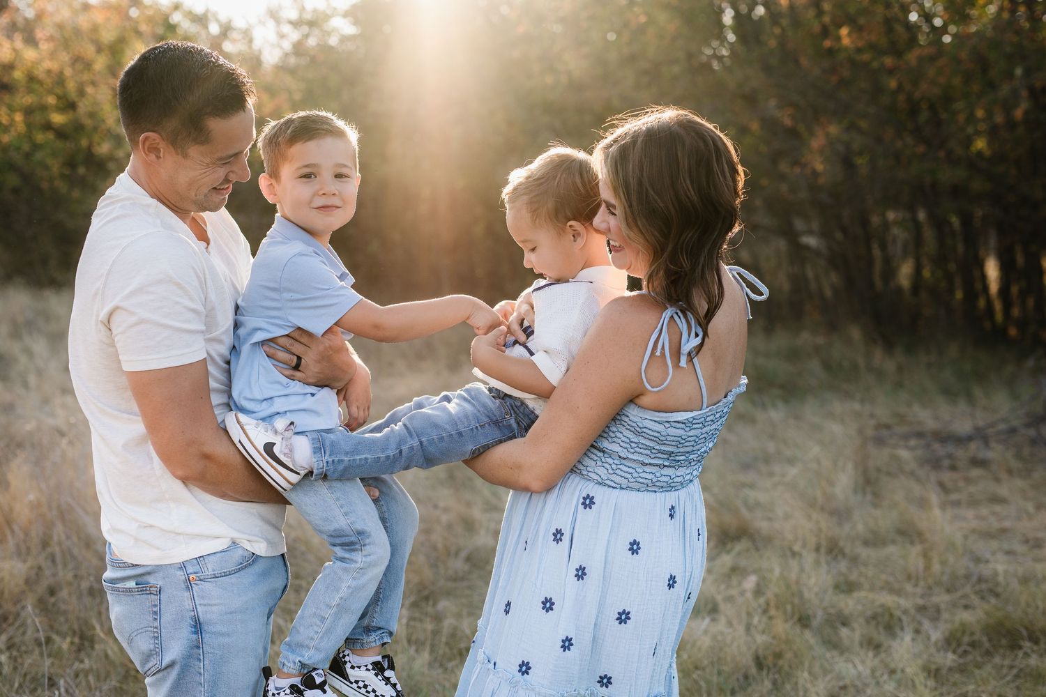 Family plays together in a sunlit field during golden hour.