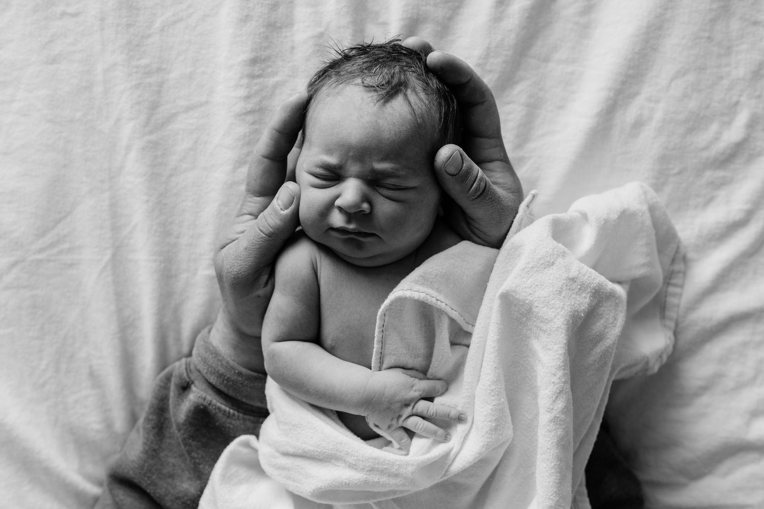 Close-up of sleeping newborn baby wrapped in soft white blanket.