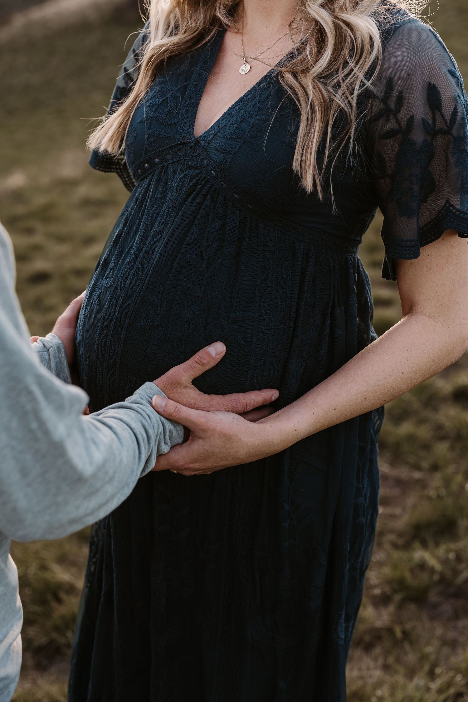 Maternity photo showing a pregnant woman in a black dress against a natural outdoor setting.