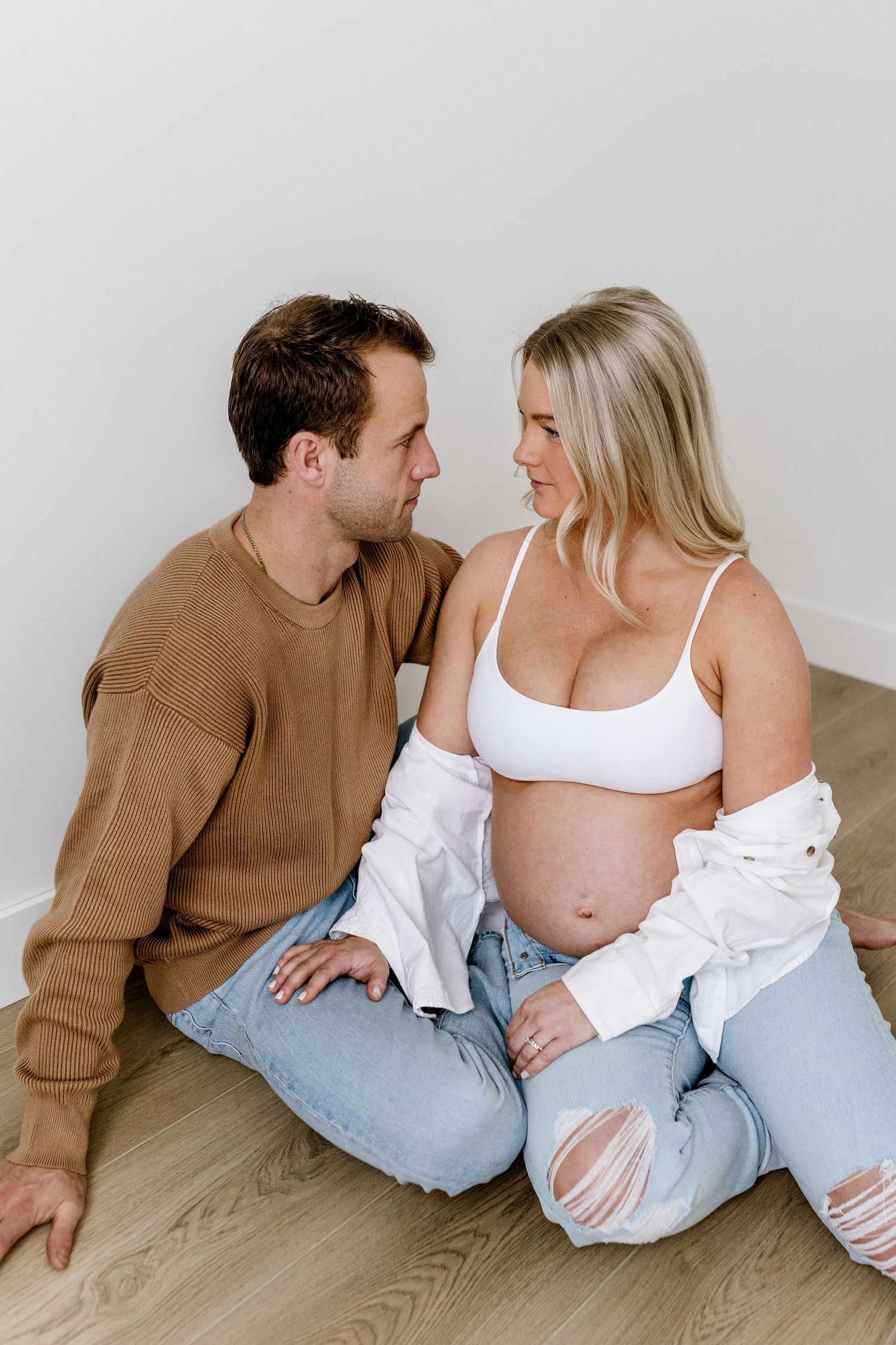 A series of intimate maternity photos showing a couple sitting together in casual clothing against a white background.